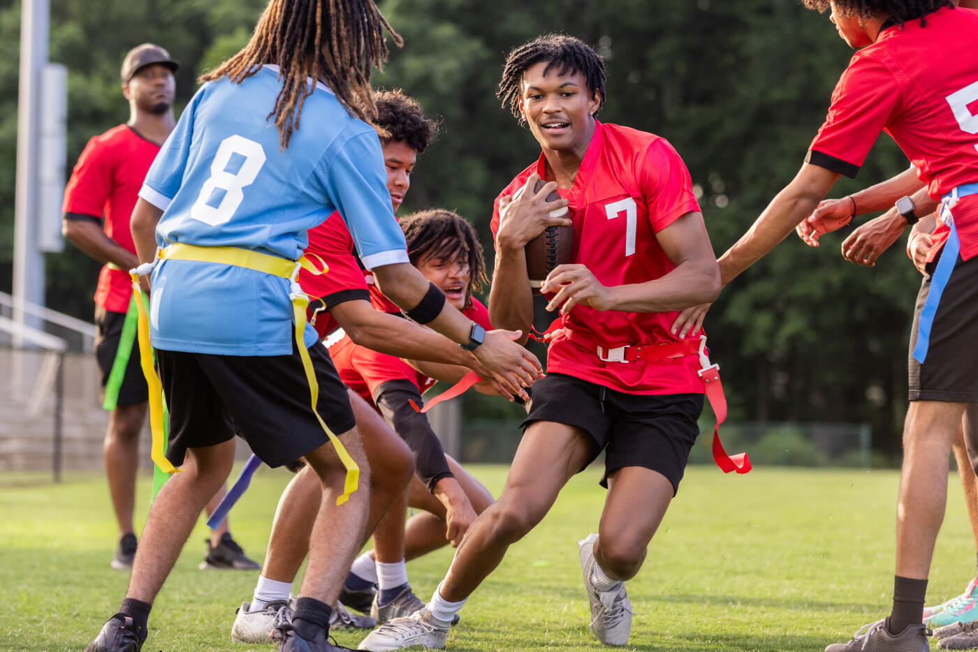 High school athlete holds ball and runs while playing flag football with his team on rural sports field