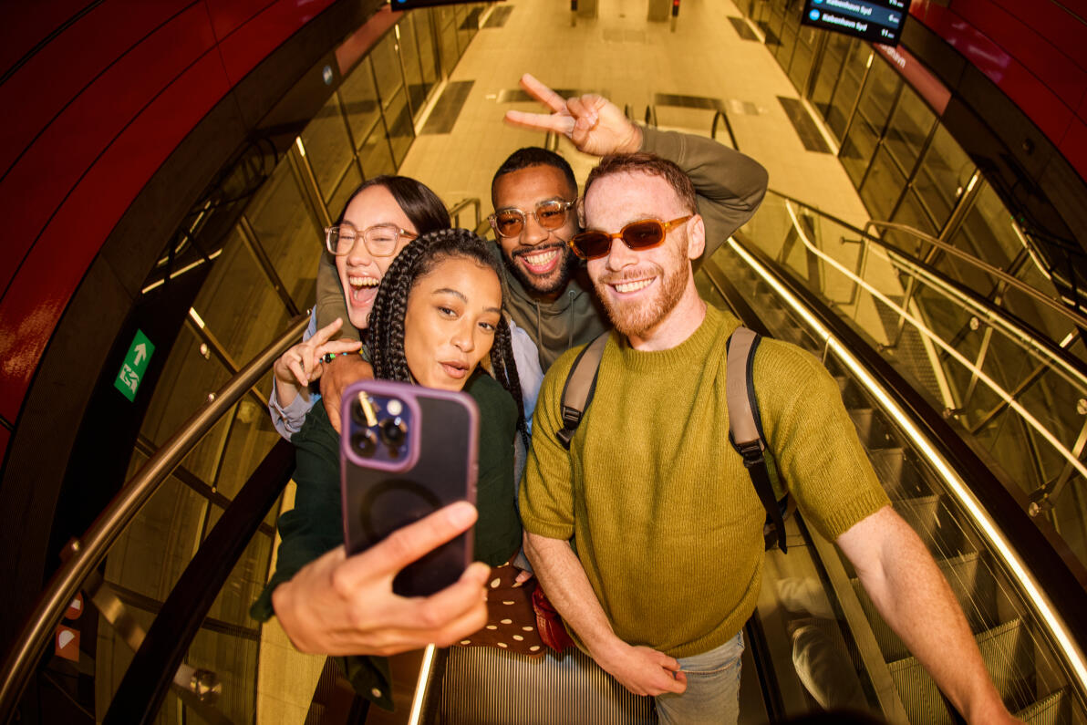 Four young adults taking a selfie while going down on an escalator