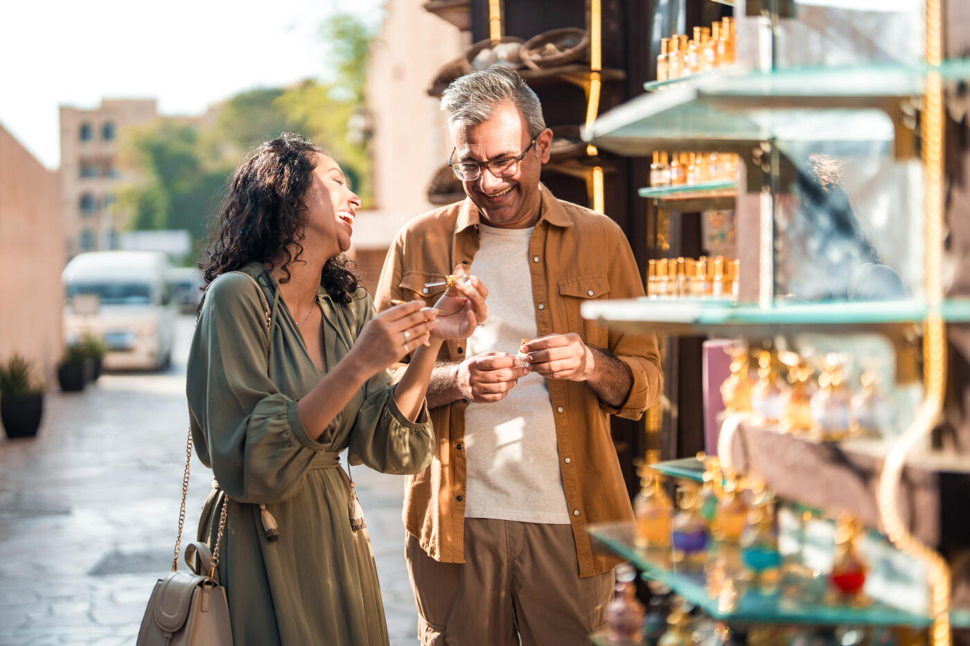 Candid portrait of mid-adult Middle Eastern woman and bearded Caucasian man sharing joyful moment while shopping at traditional bazaar with illuminated store displays in background.