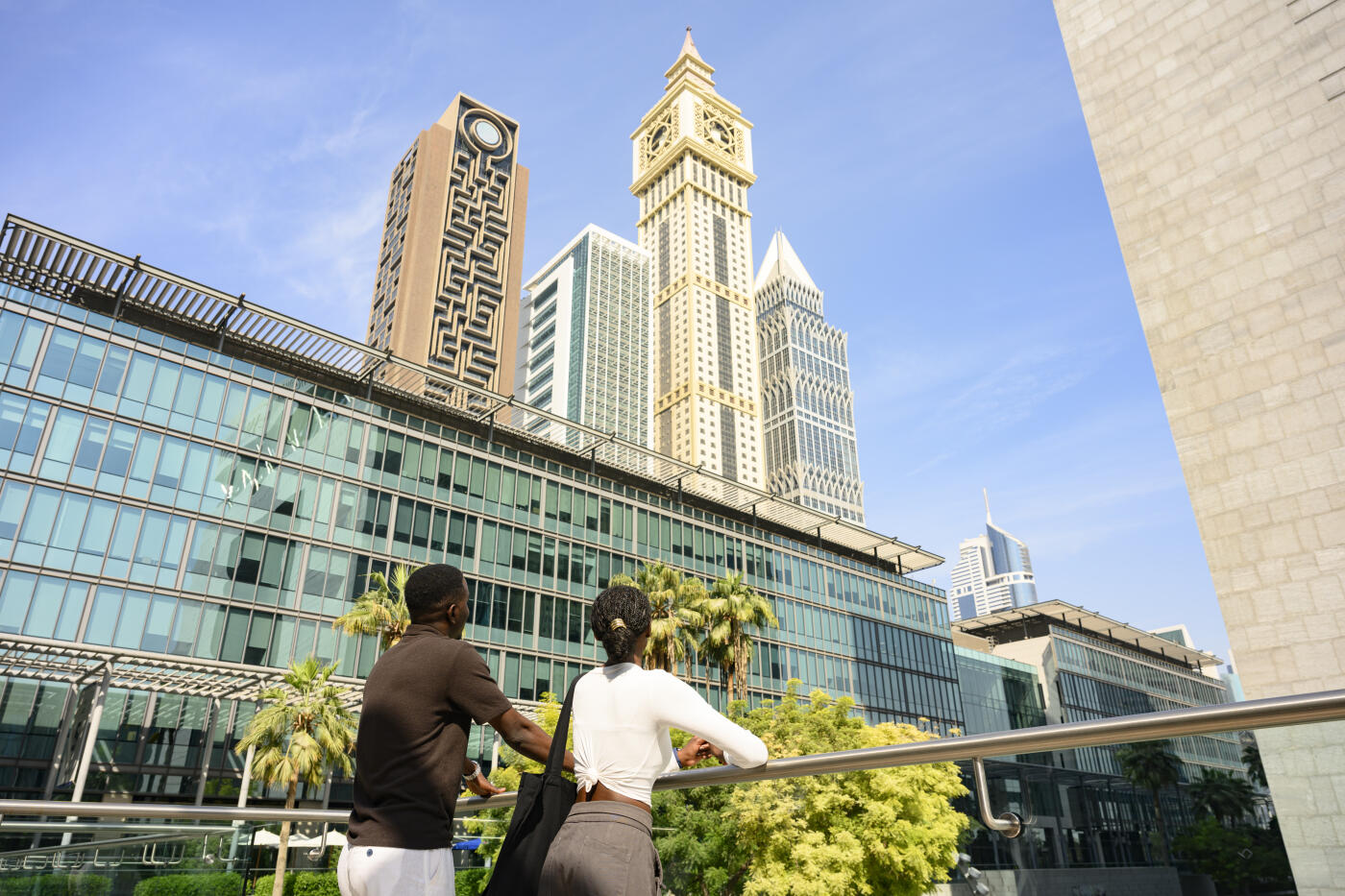 Couple holding hands and looking up at Dubaiâs modern skyscrapers and Al Yaqoub Tower, enjoying a sunny city break and urban architecture in downtown Dubai