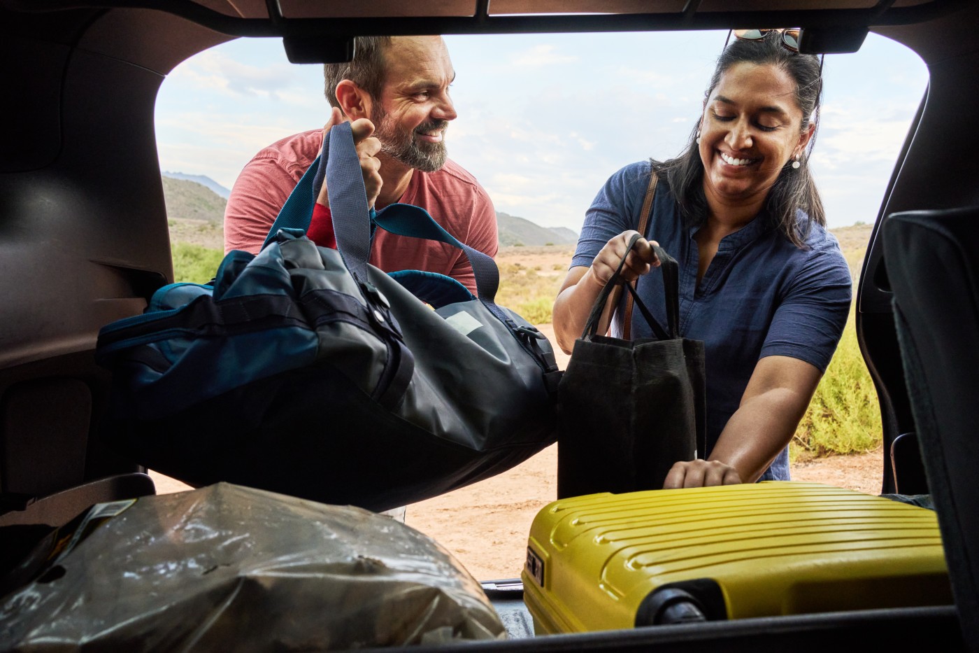 Smiling friends packing their bags into the trunk of their car after a summer vacation together in a nature reserve