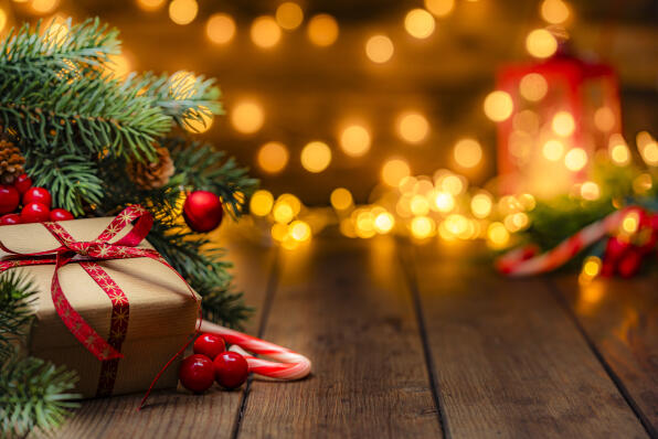 Christmas present wrapped with craft paper and red ribbon under the Christmas tree in a cozy festive atmosphere with defocused Christmas lights at background