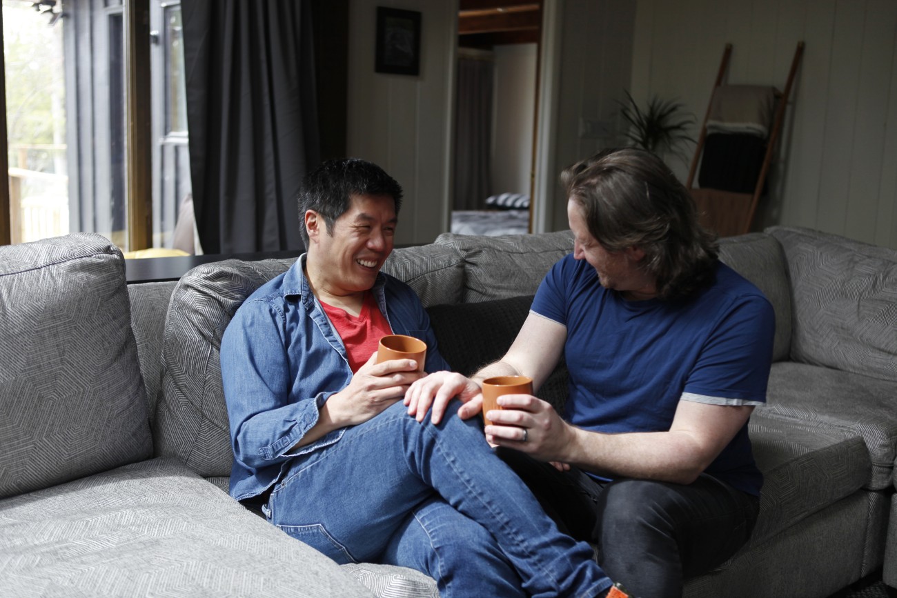 Mannelijk stel op de bank in de woonkamer met kopjes in de hand, oprecht