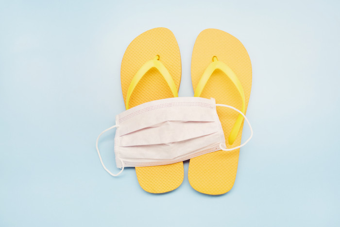 Still life of a white face mask and orange flip-flops on blue background, on vacation with a protective face mask