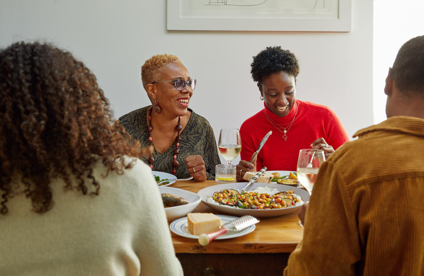 Group of mixed aged relatives sitting at dining table enjoying home cooked meal talking and laughing, togetherness, healthy eating, meal time, domestic life