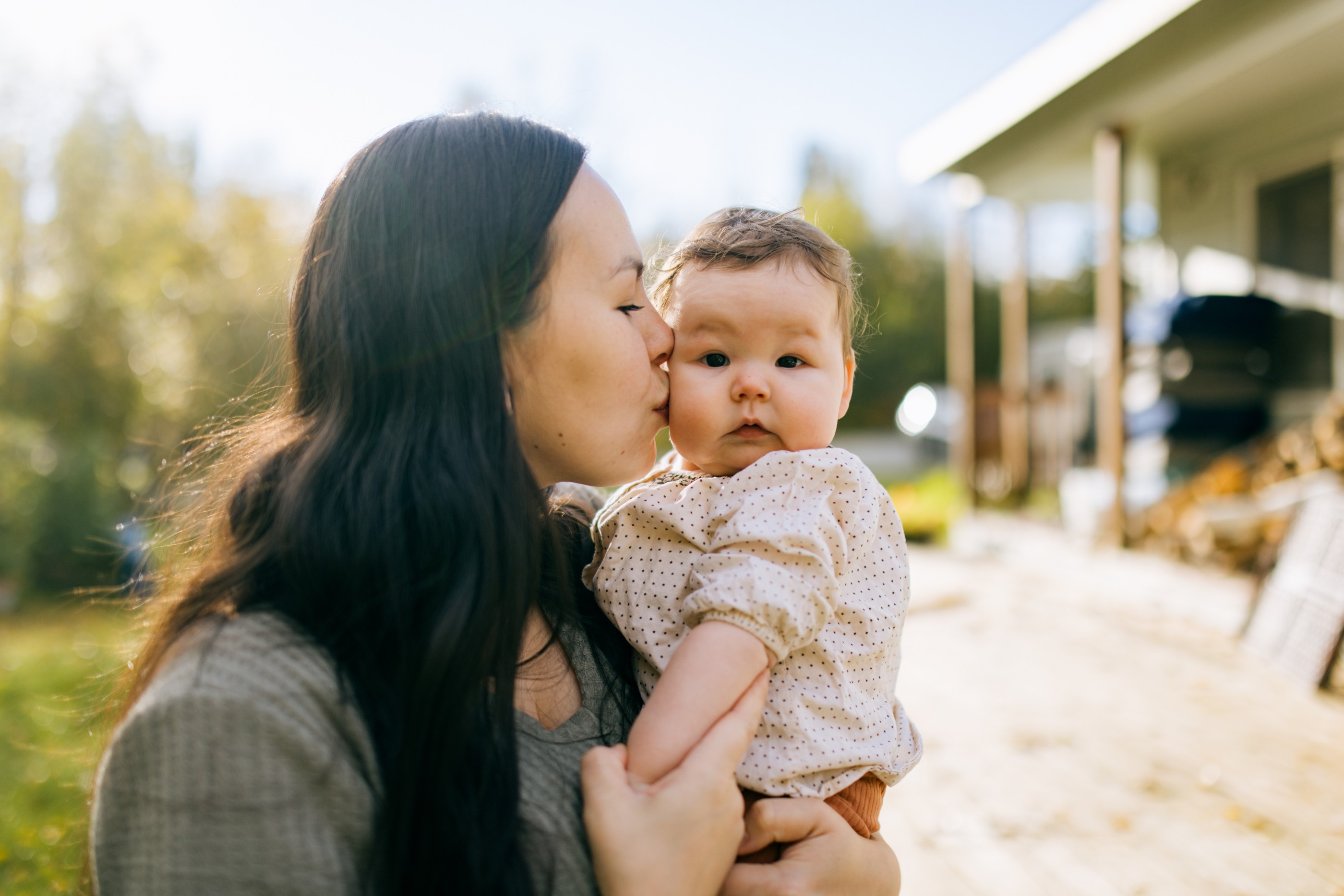An Indigenous North American woman spends time bonding with her sweet baby girl in their yard, the house visible in the background.  Shot in Palmer, Alaska, USA.