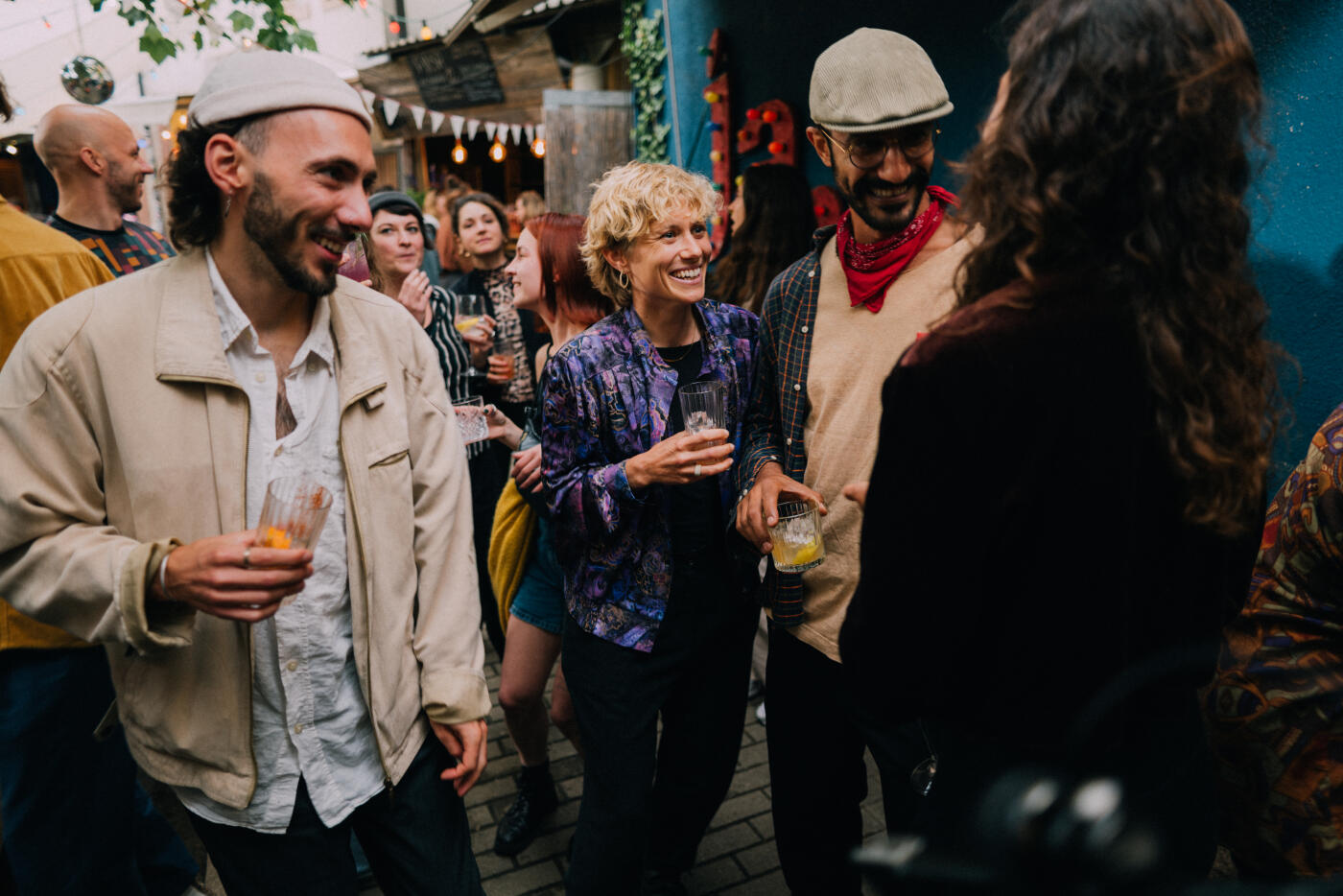A vibrant gathering of friends in a festive outdoor setting, socializing over drinks and laughter, surrounded by an enthusiastic crowd. Capturing the spirit of camaraderie and celebration. Part of a series with video
