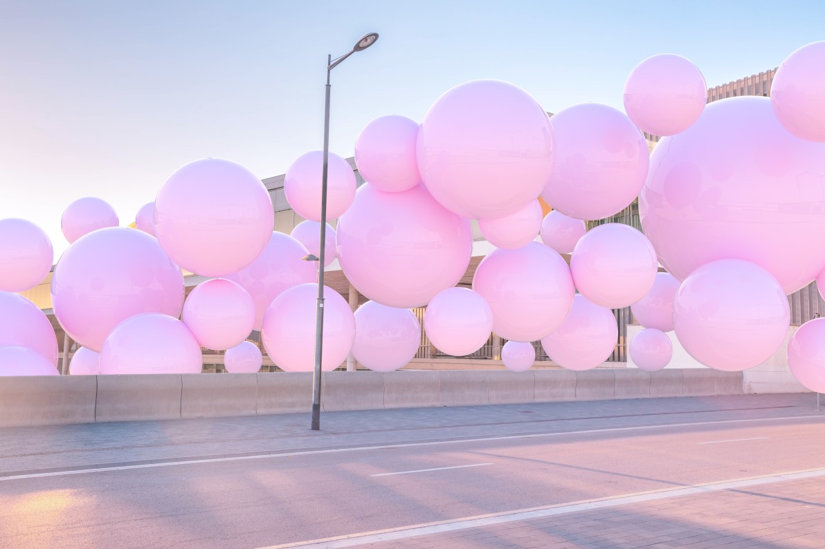 3D digital image of large group of pink balloons flowing like a mass in the modern urban street with empty road.