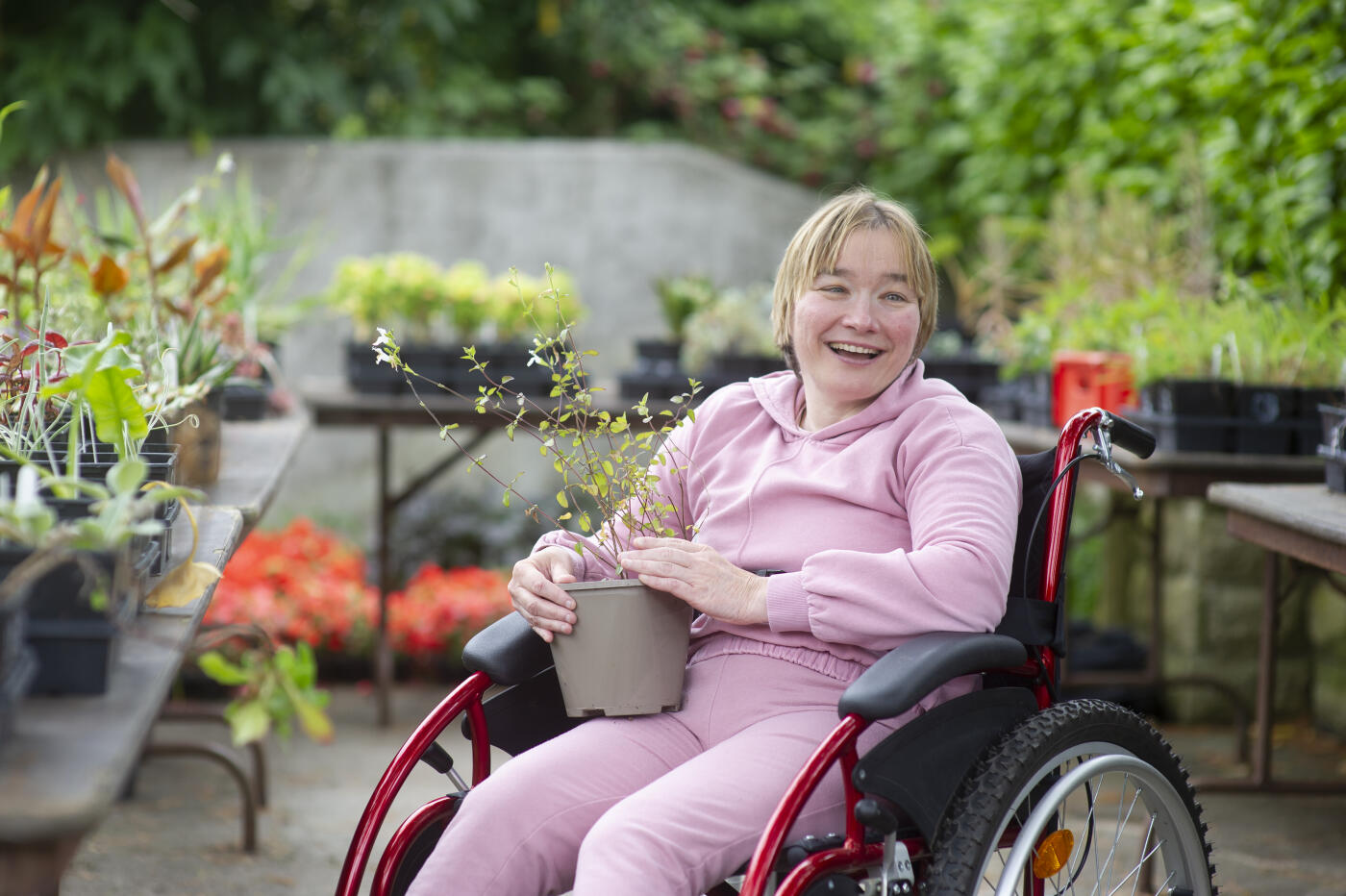A woman holding a plant from a community garden. She has quadriplegic cerebral palsy and is a wheelchair user.