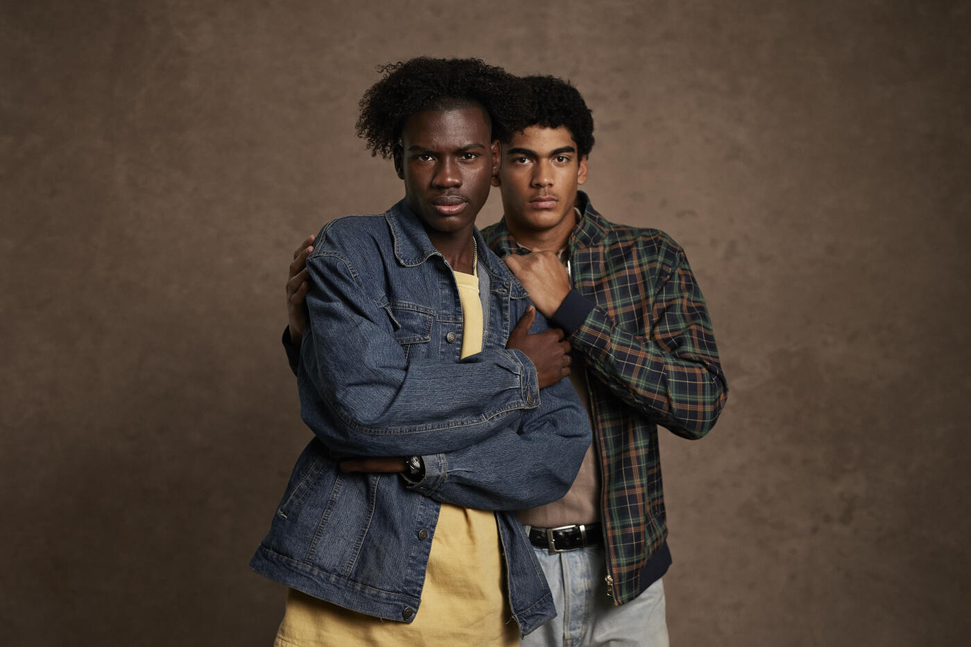 Portrait of young man standing with arm around friend against brown background