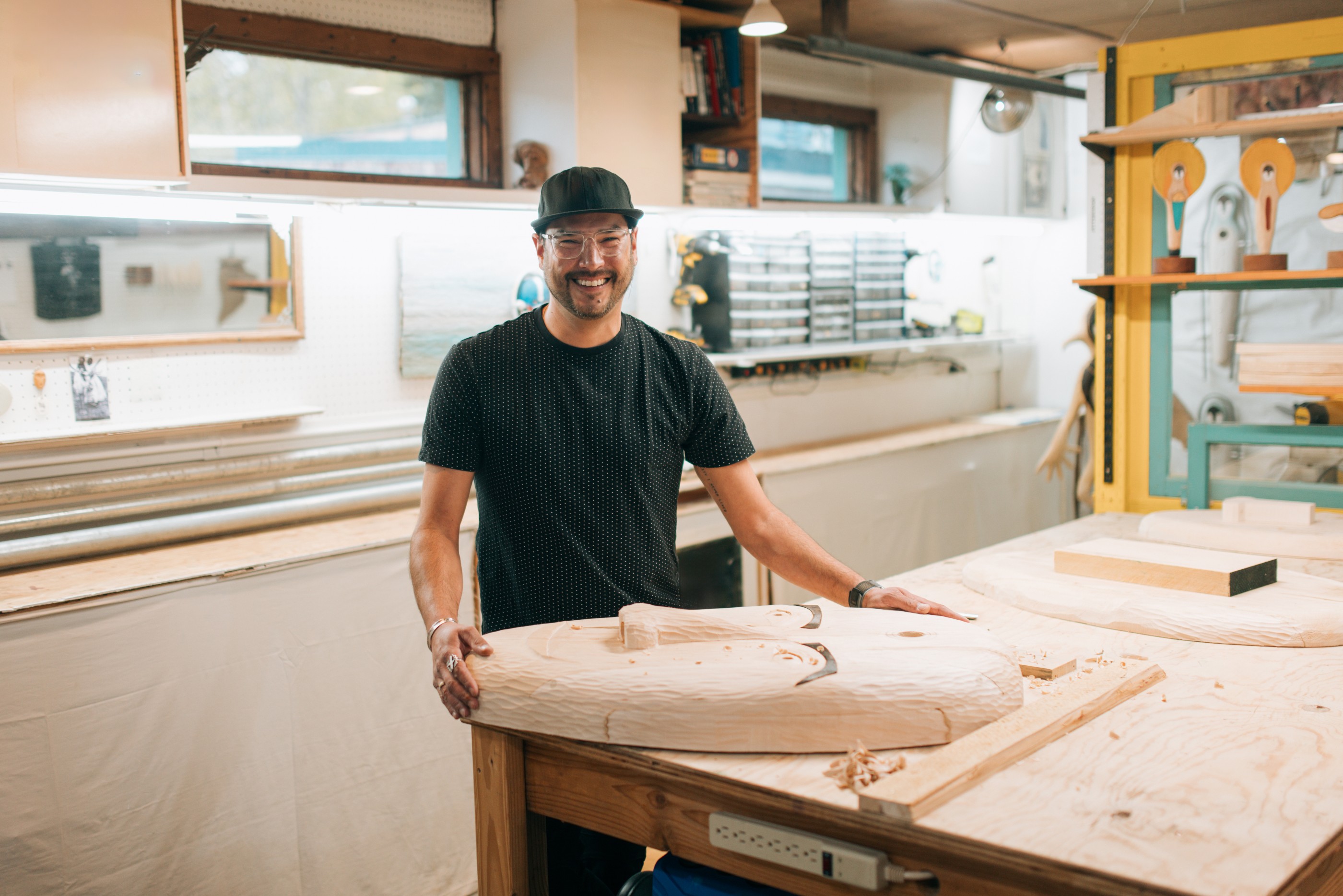 A multiracial Alaskan man in his workshop, planning, carving, and networking online with his hand carved wooden masks.  Traditional culture with a modern twist.