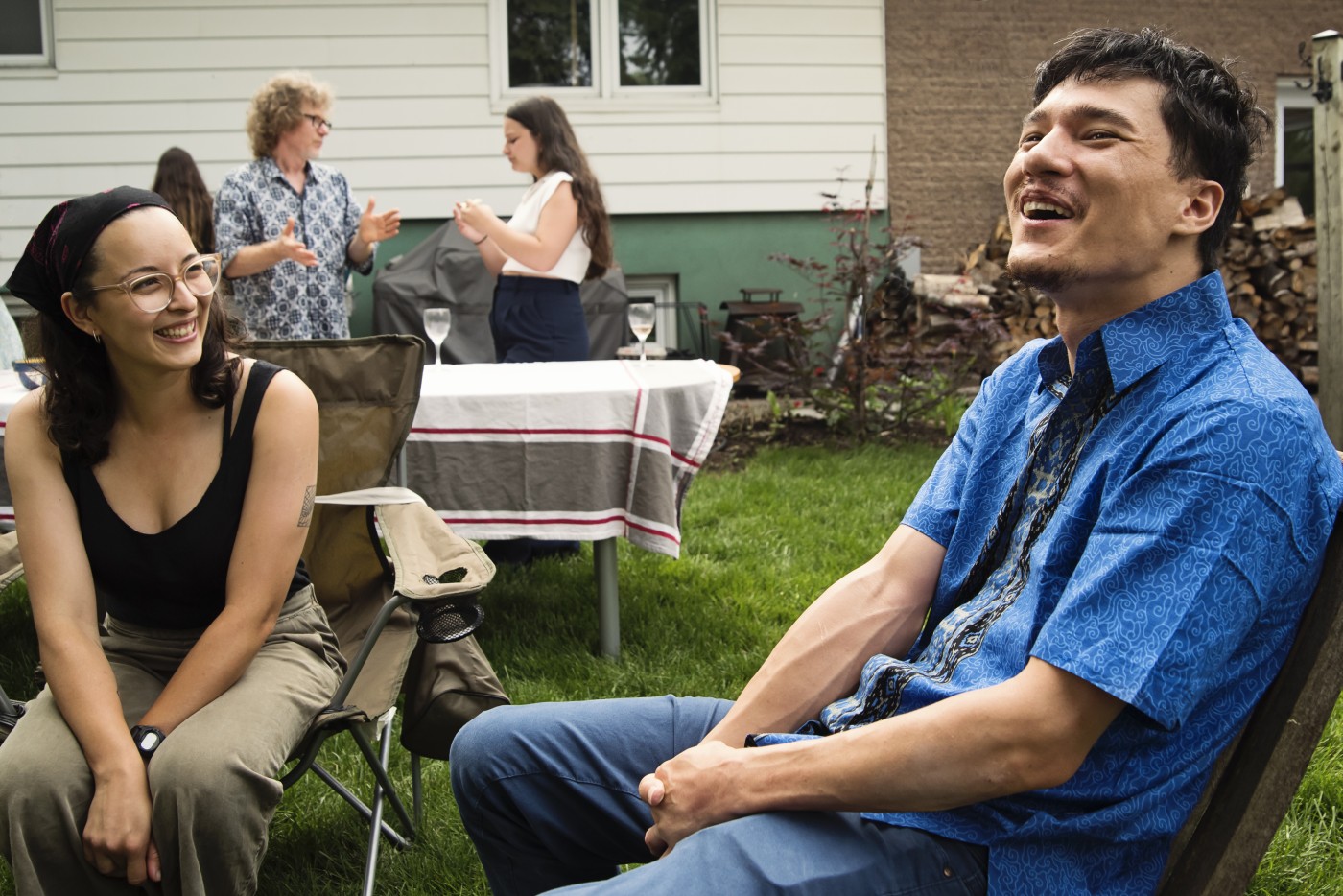 Multiracial young adult in a garden party in summer. He is living with a disability, cerebral palsy, and is wearing an indonesian printed blue shirt. He is chatting with family members. Horizontal waist up outdoors shot with copy space. This was taken in Quebec, Canada.