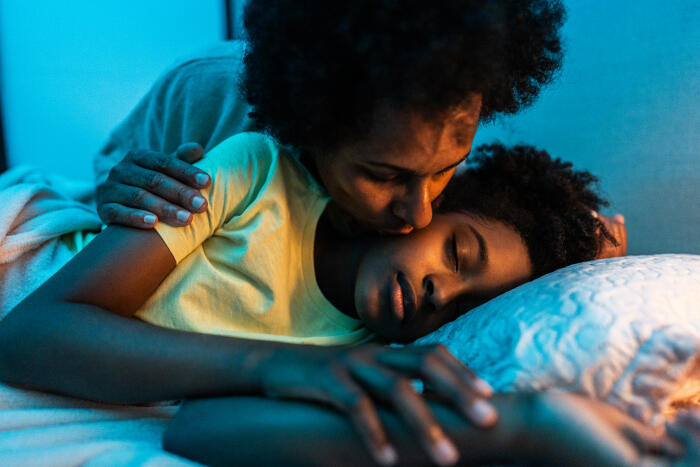 Mother kissing her daughter while she's sleeping in the bedroom at home