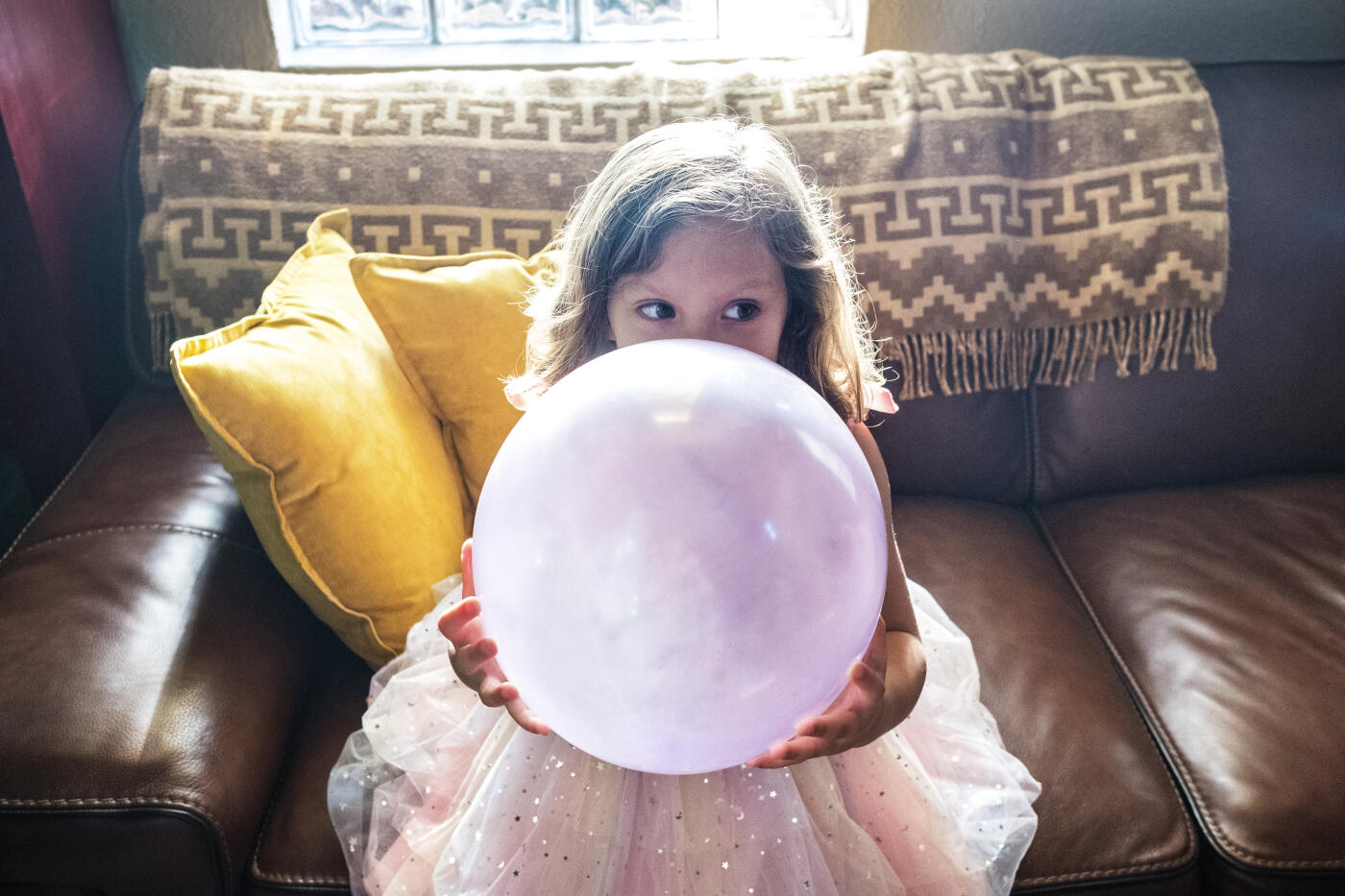 5 year old girl hiding behind a balloon at her birthday party.