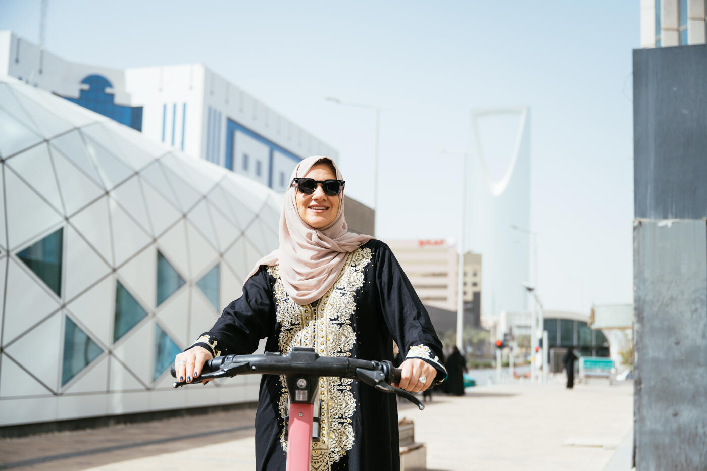 Smiling Arabic woman using electric scooter in the downtown