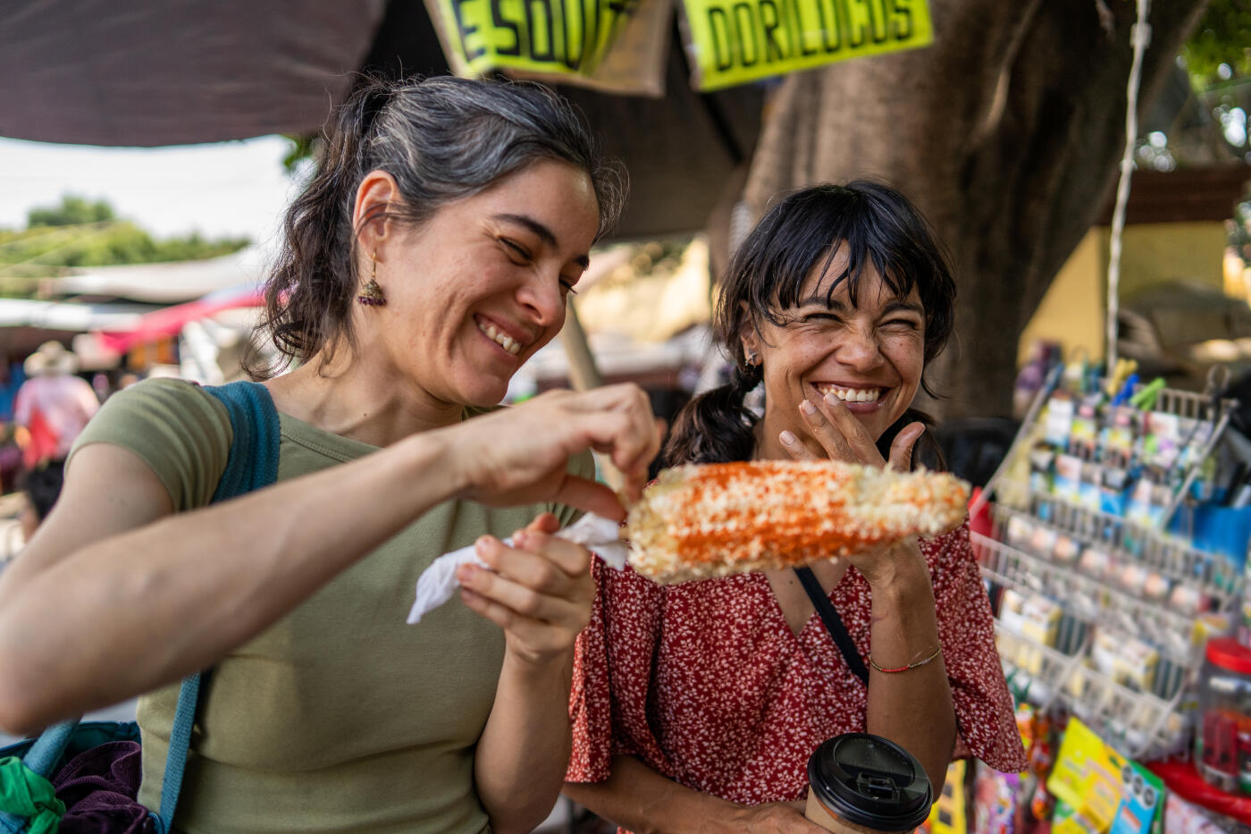 Two female friends having street food, elote, in a mexican outdoor market
