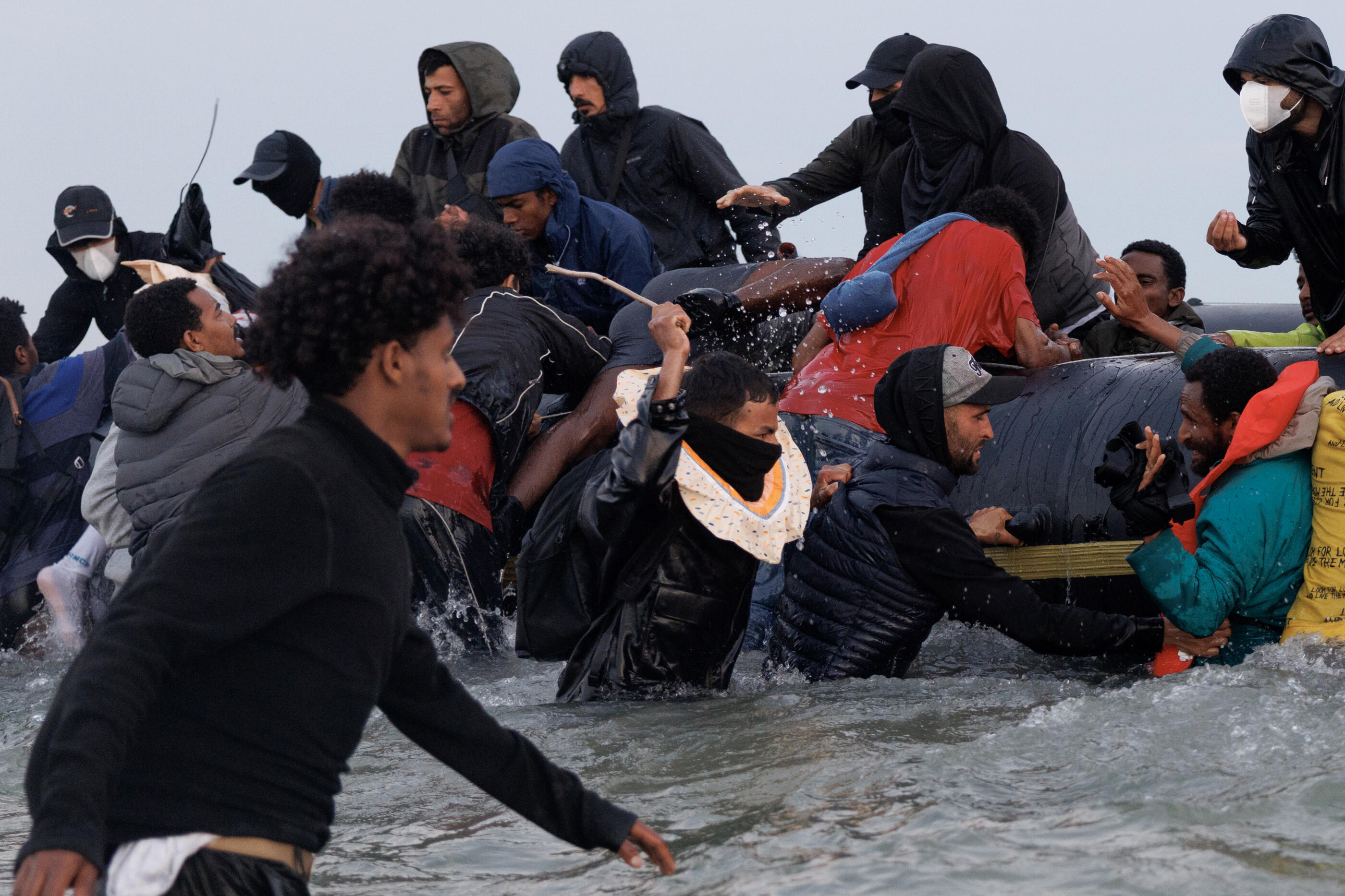 GRAVELINES, FRANCE - JULY 02: Traffickers, (with their faces covered) try to manage the scene using sticks as migrants wade into the water to be collected by a small boat at sunrise on July 02, 2025 in Gravelines, France. Last month, it was reported that French officials were planning changes to policies that govern interceptions at sea, allowing police to intercept small boats within 300 metres of the French shoreline, in a bid to curb migrant crossings of the English Channel. The move, which has not been confirmed, would be welcomed by UK authorities, who see it as a step toward stronger border enforcement. (Photo by Dan Kitwood/Getty Images)