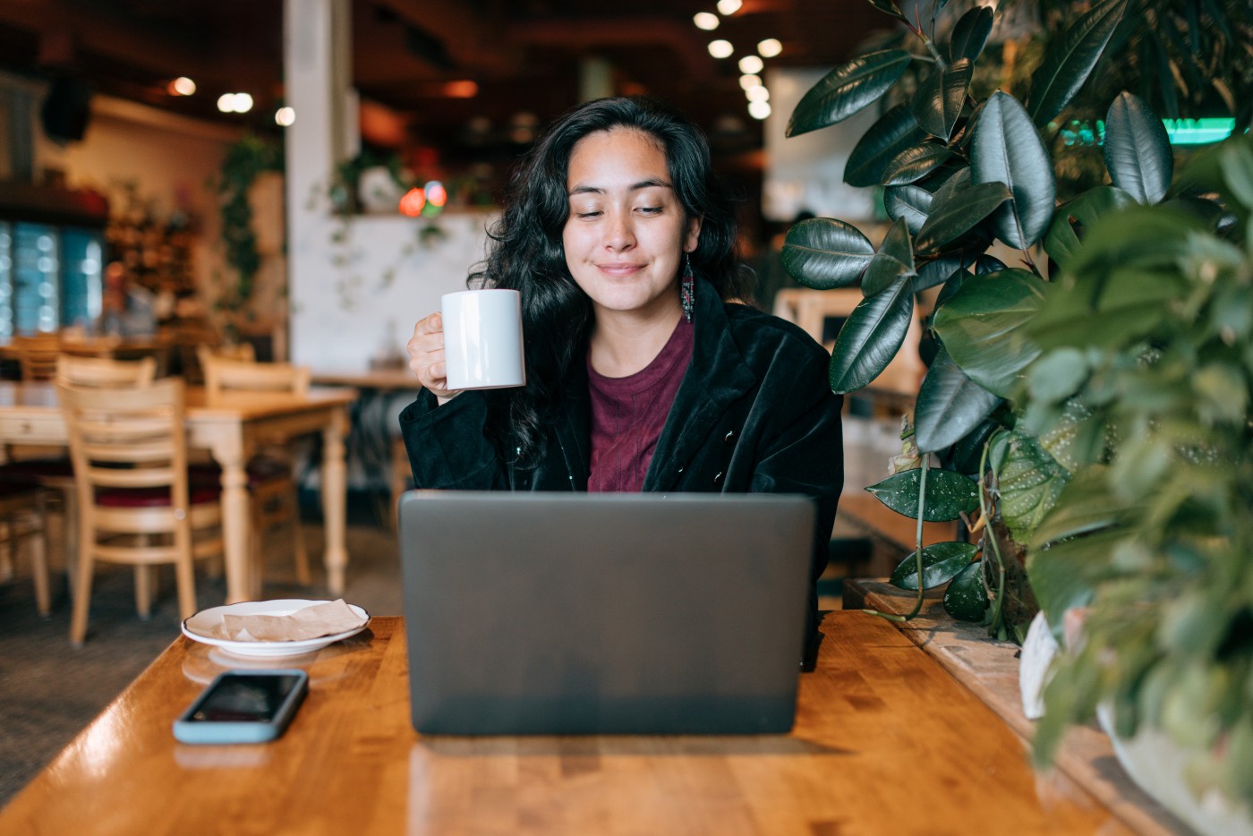 An Indigenous Alaskan woman works at a favorite coffee shop, using her laptop computer for online job or studies.  Shot in Anchorage, Alaska, USA.