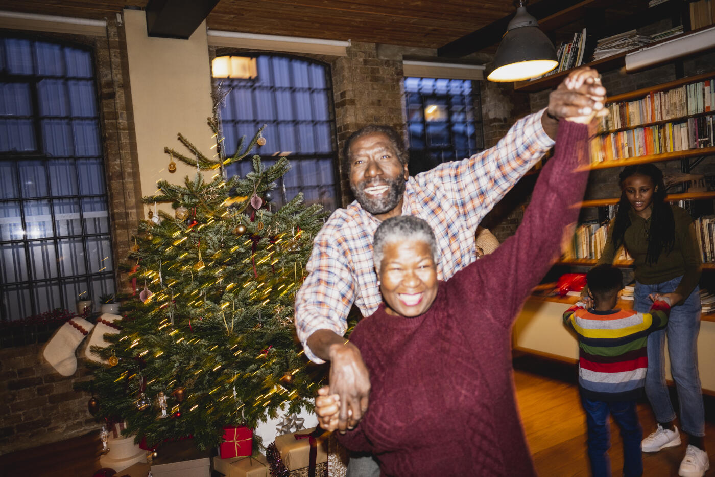 Focus on grinning man and woman having fun in loft apartment with grandchildren learning in background. On-camera flash, retro-style photographic effect.