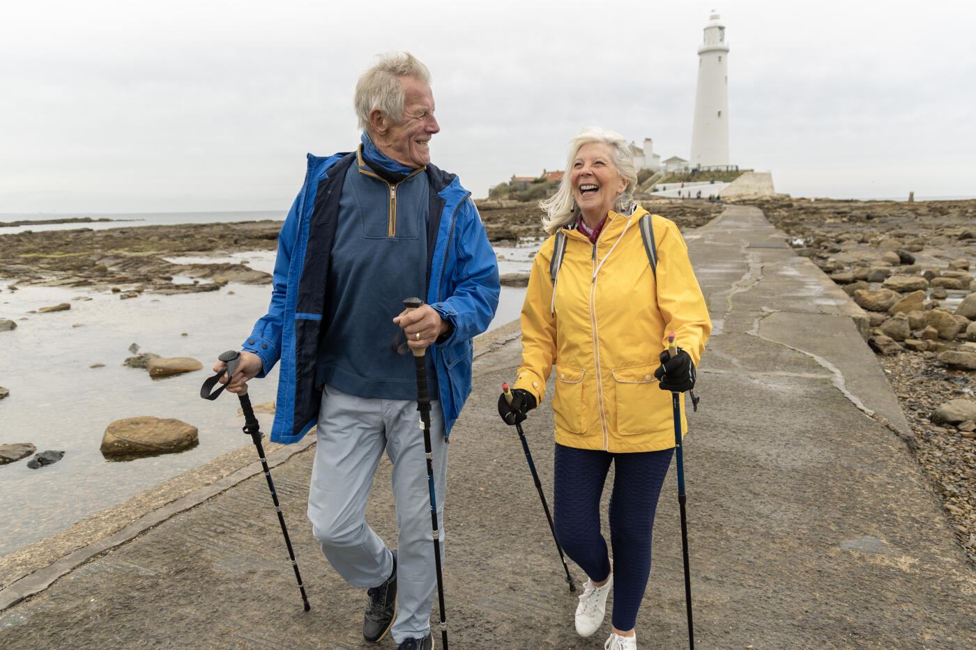 Senior retired couple walking on a causeway beside the Tynemouth lighthouse on a day out together on the Northumberland coast