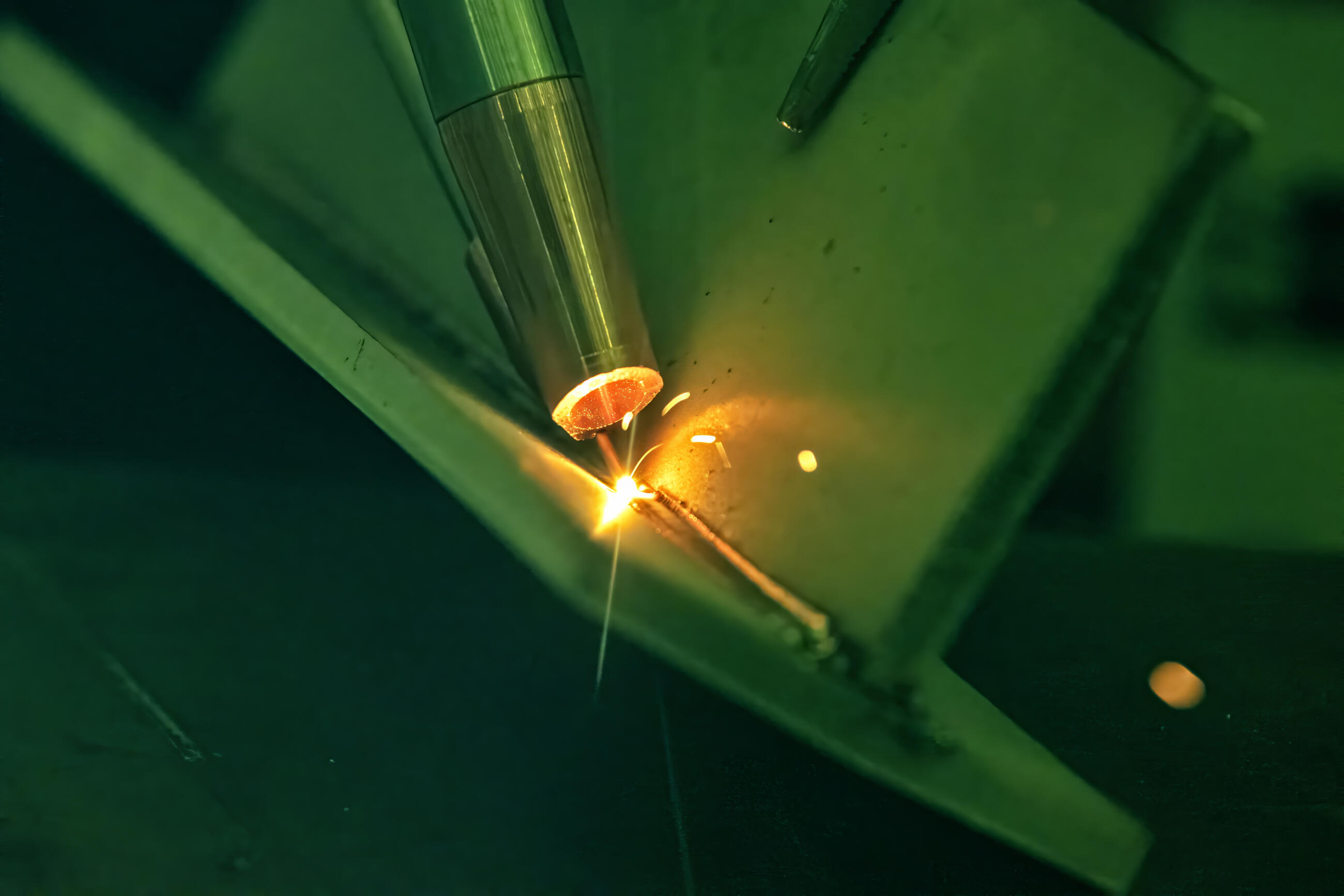 Automated robotic welding torch arm precisely fusing a metal joint structure with intense bright electric arc flash and golden sparks in an industrial fabrication factory.