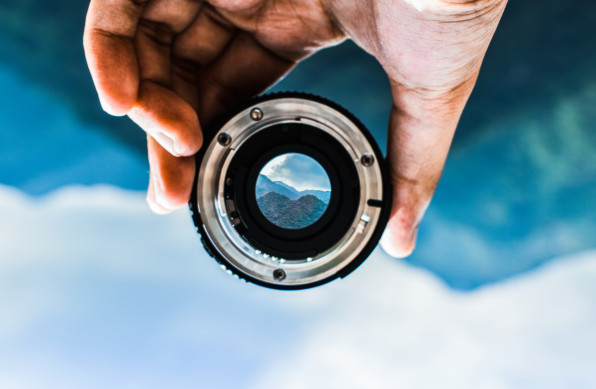 Upside Down Image Of Person Holding Camera Lens Against Mountain