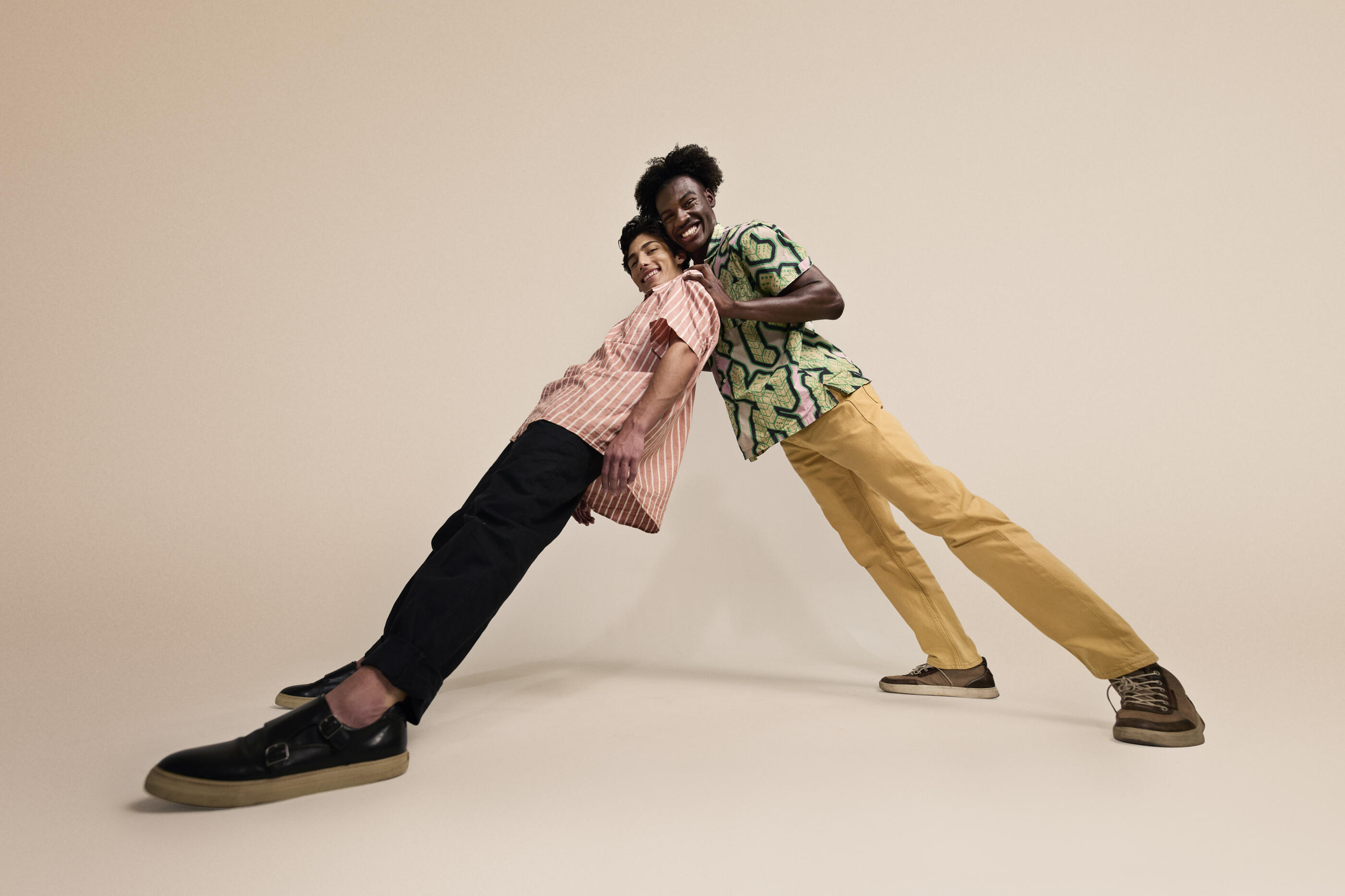 Low angle view of smiling male friends leaning on each other against beige backdrop
