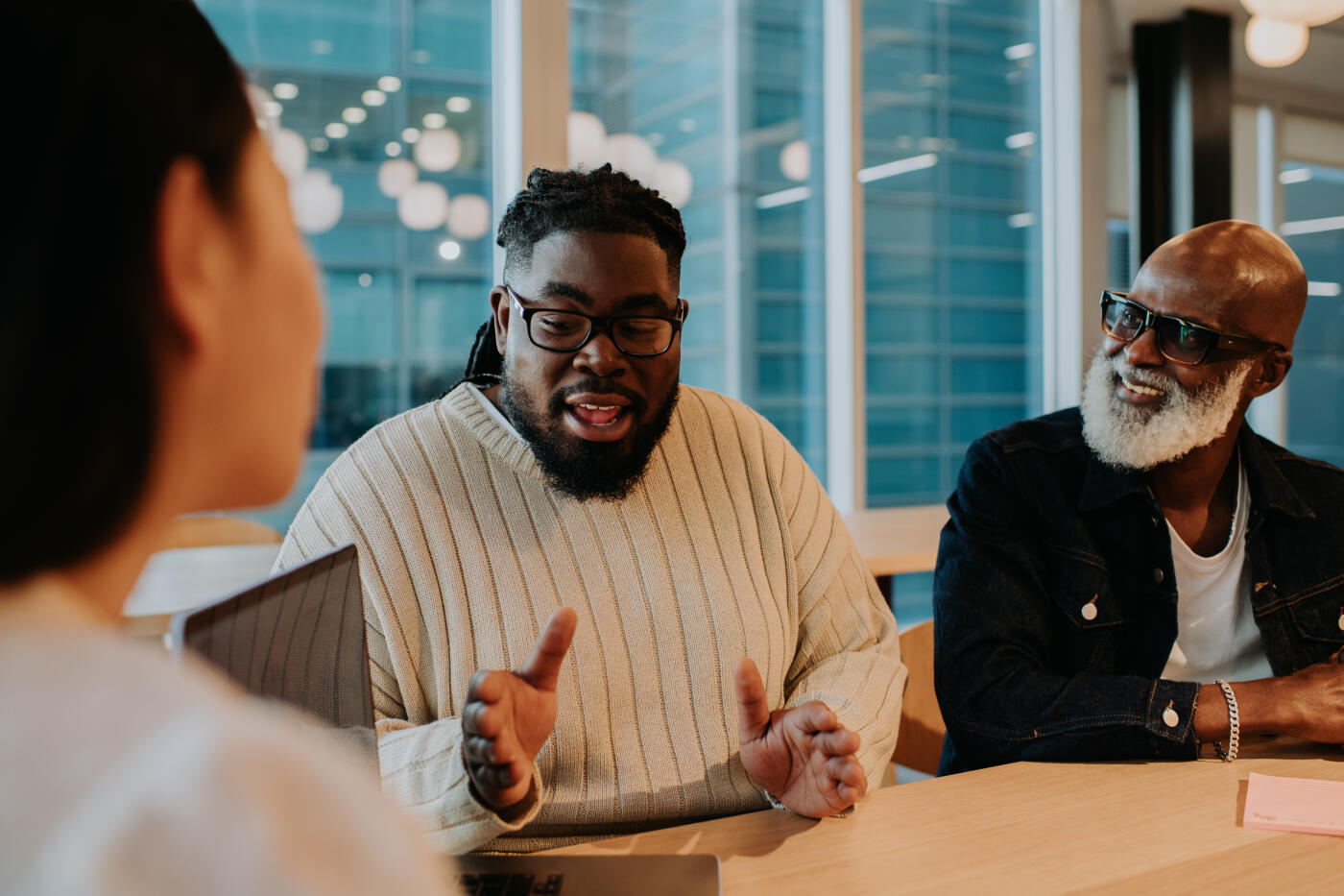 A young employee has a discussion in a meeting room with colleagues. The participants look engaged and interested.