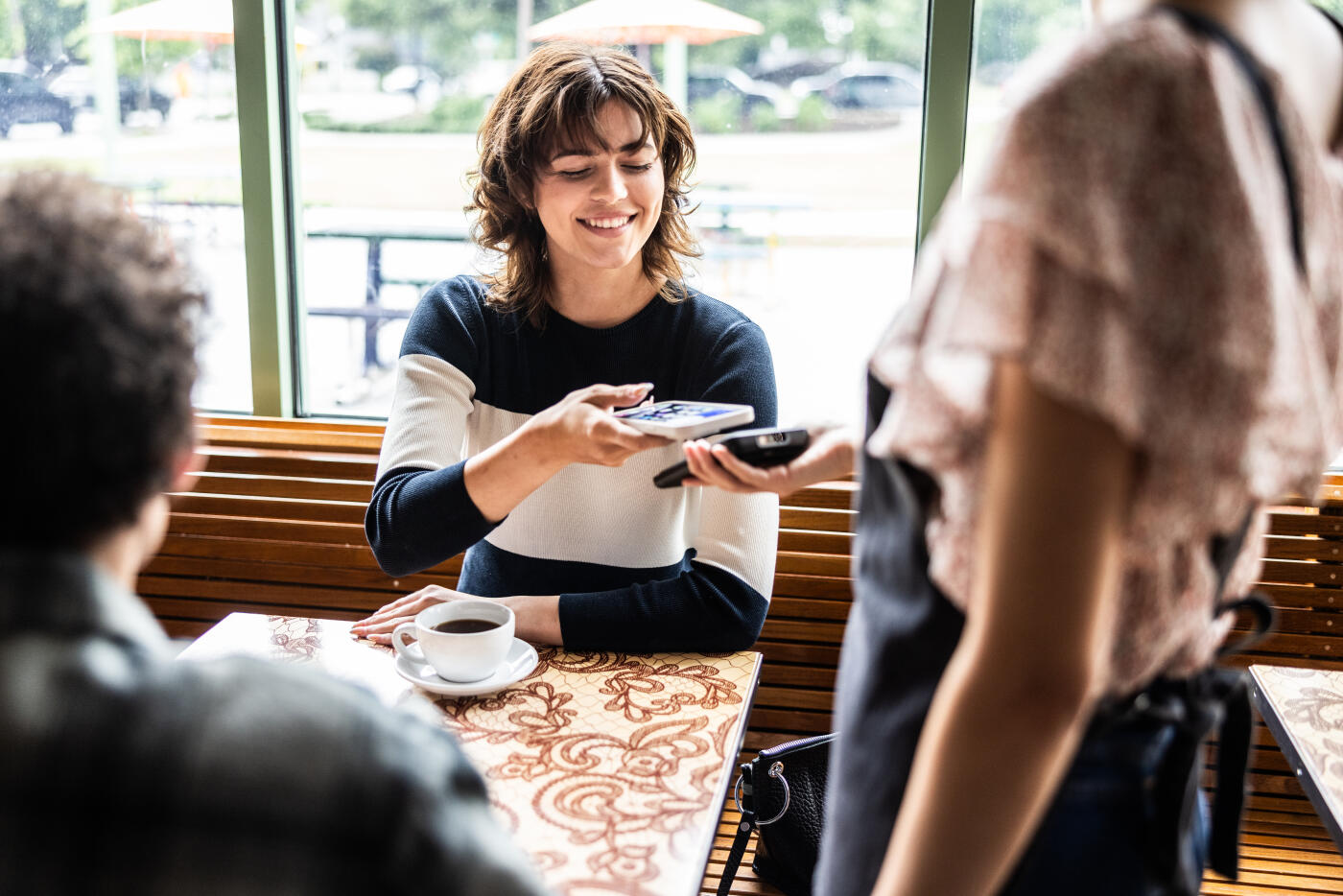 Young woman paying her bill with a smartphone in coffeeshop
