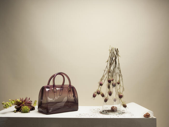 Transparent handbag on table surface with plants, grass and soil around it