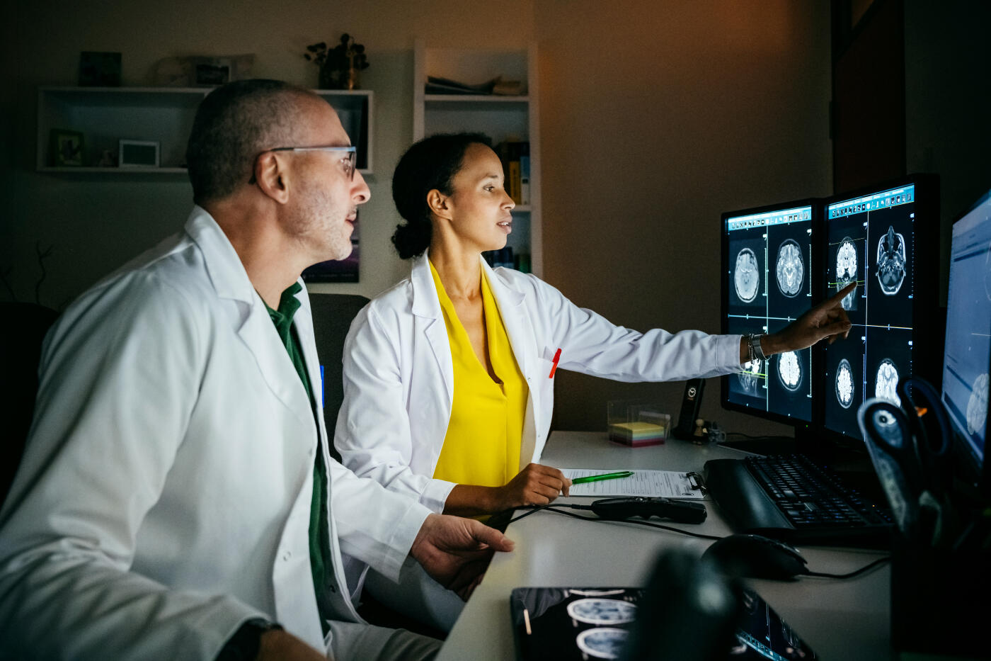 Two doctors looking at computer monitors and discussing a patient's injury following a CT scan.