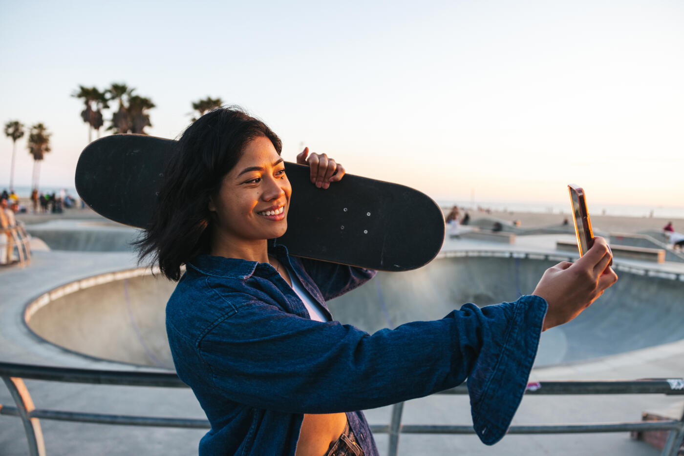 Young woman with a skateboard take a selfie by the skate park by the beach.