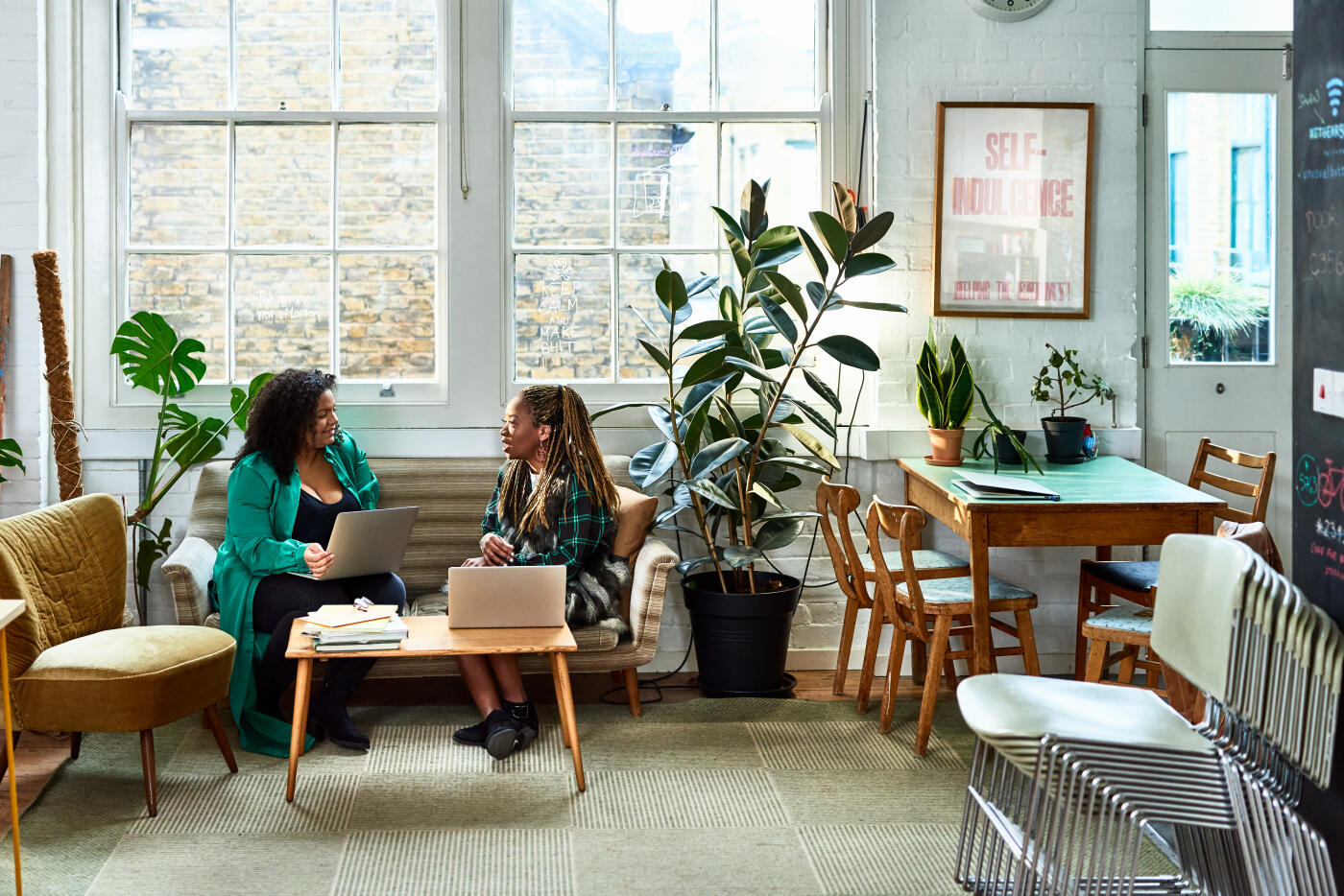 Female colleagues sitting on couch in discussion in breakout meeting area, collaboration, teamwork, planning