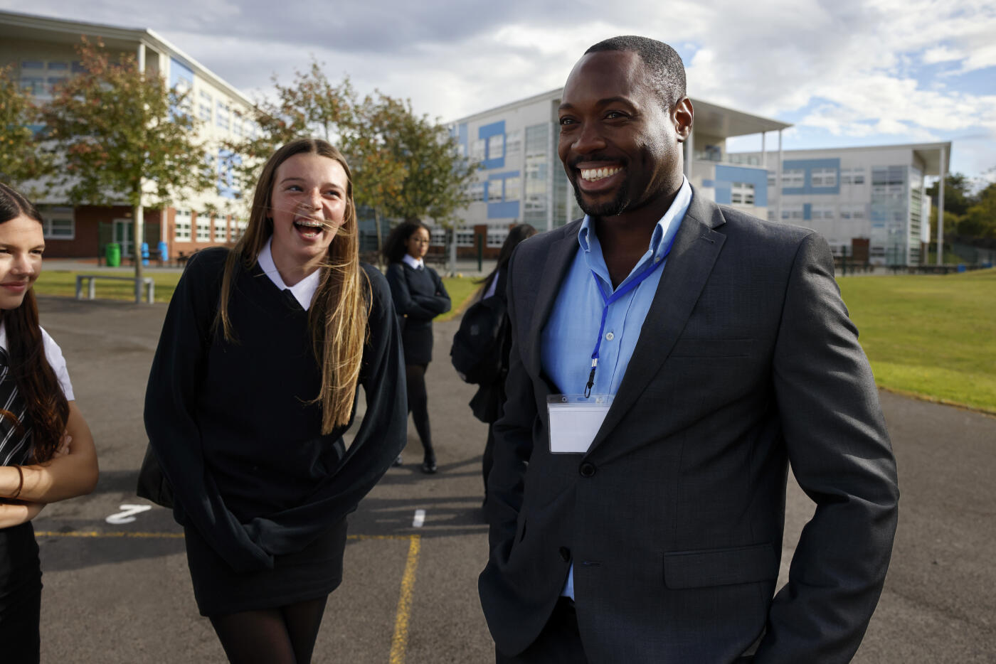 A group of female secondary school students enjoy break time outdoors, laughing and chatting with their teacher. The image highlights positive relationships, connection, and engagement between students and staff, reflecting a supportive and friendly school environment.