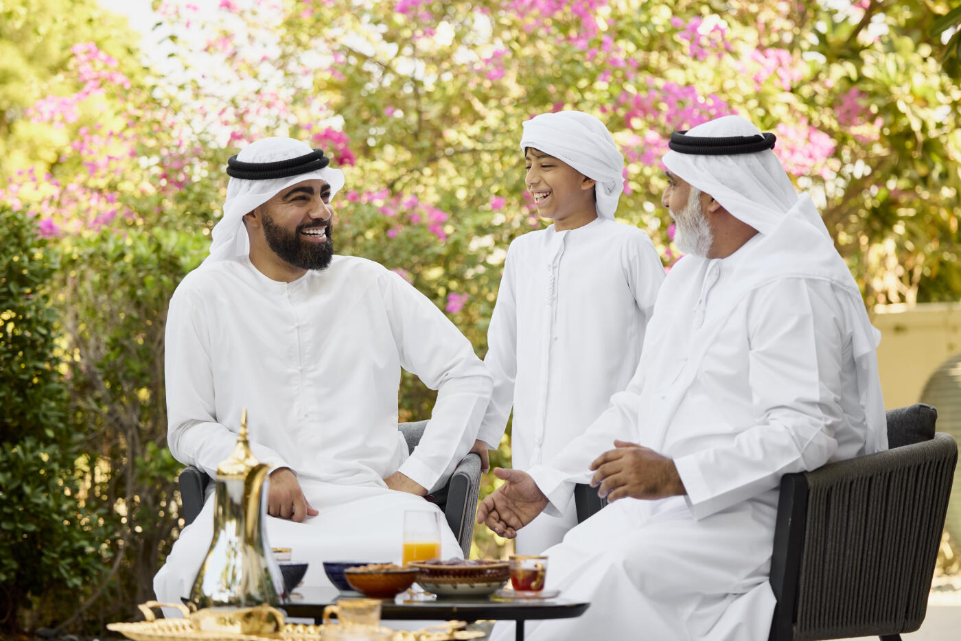 Happy Emirati boy laughing while spending leisure time with family. Middle eastern people are enjoying with each other. Refreshments are kept on table.