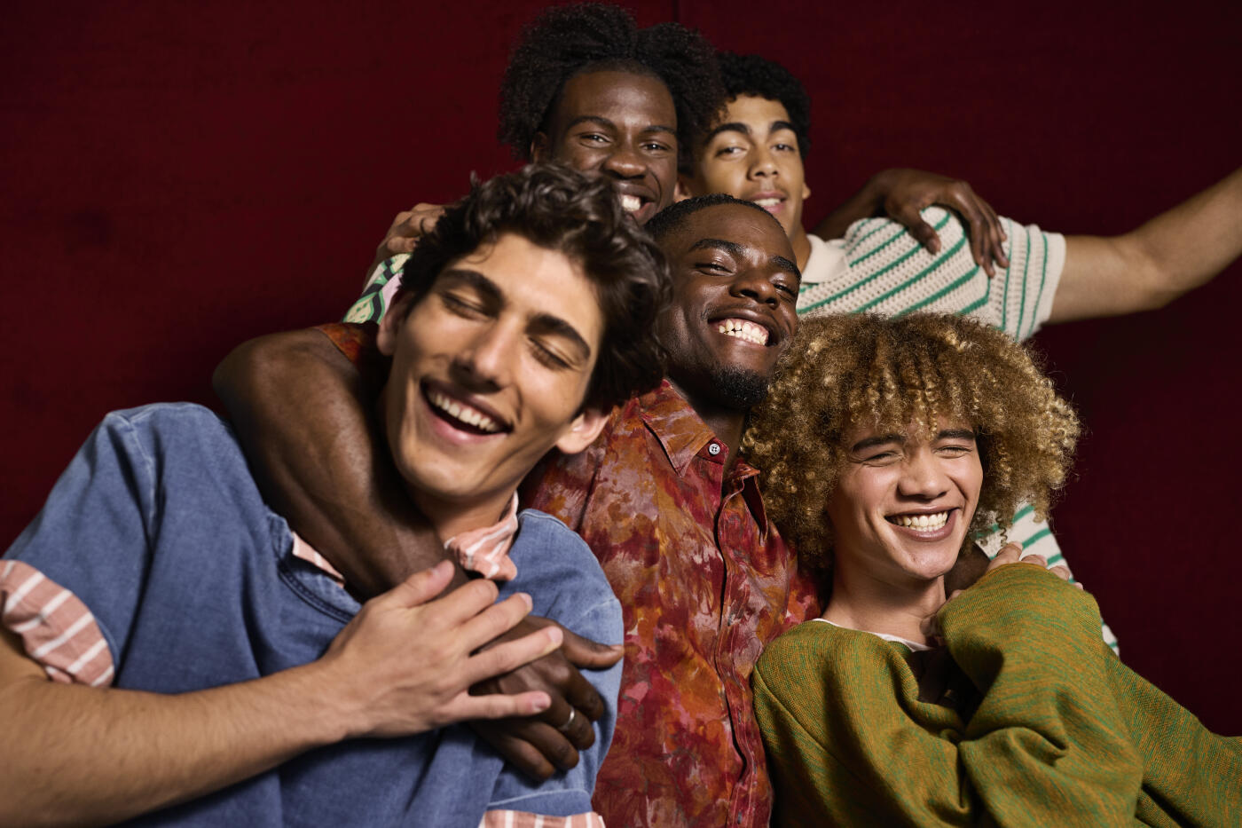 Carefree young man enjoying with arm around friends against maroon background