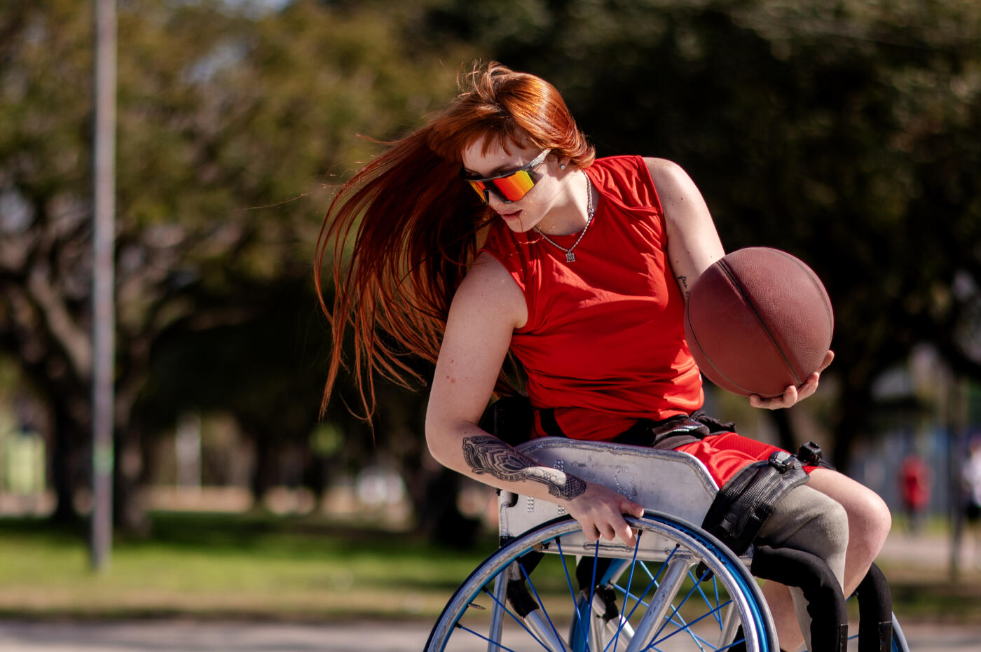 woman with red hair with a leg prosthesis, practices basketball shooting hoops in her wheelchair