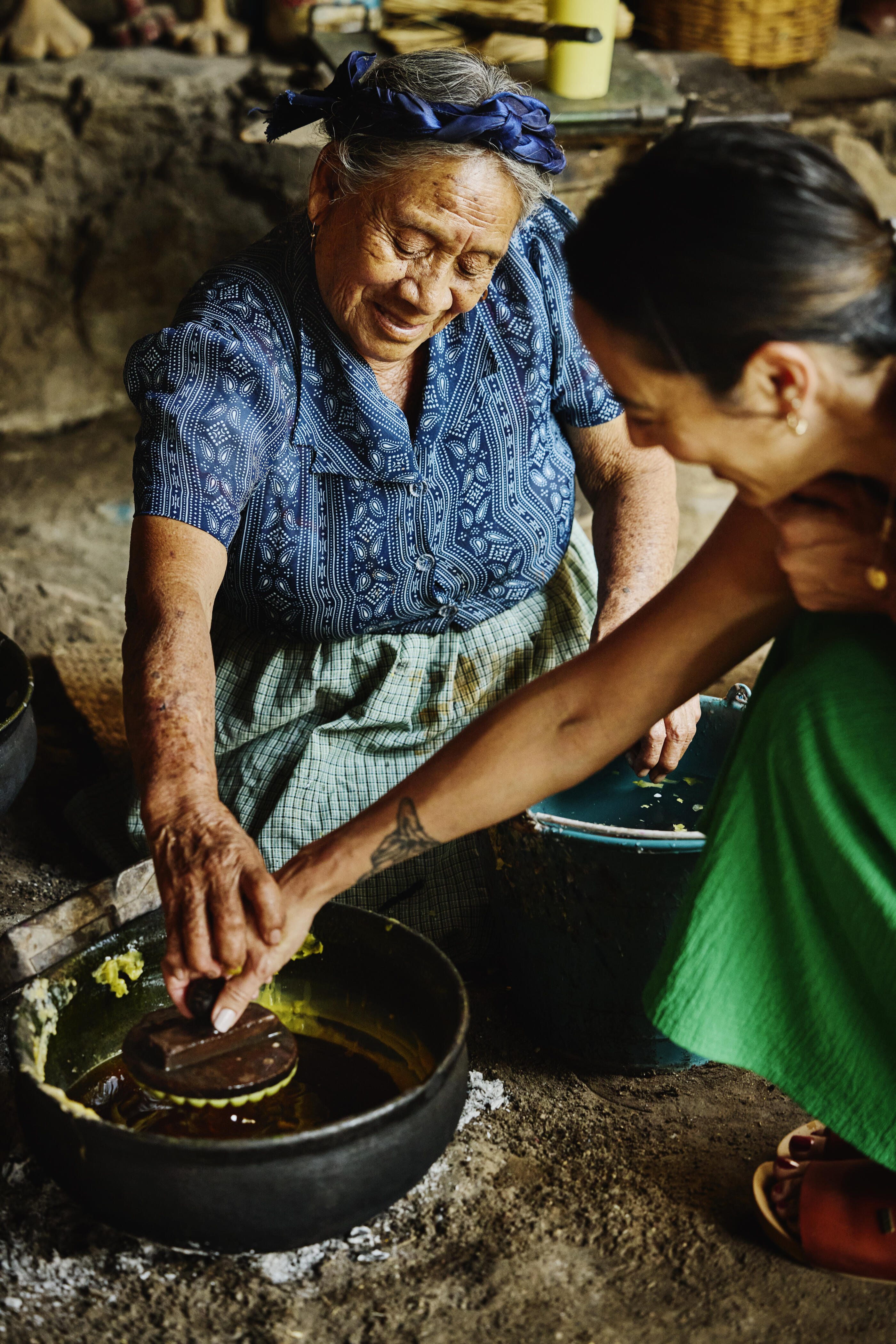 Medium shot of smiling senior artisan assisting mature female tourist through traditional Oaxacan candlemaking class during her Mexican vacation