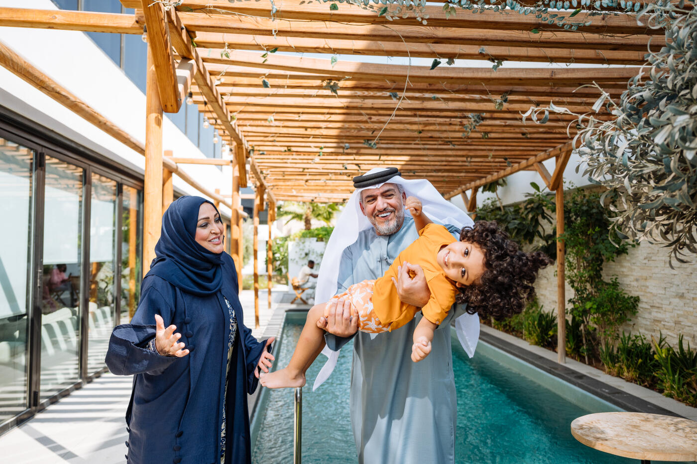 Middle Eastern parents with little boy enjoying holiday in luxury villas with swimming pools, family playing with the cheerful boy