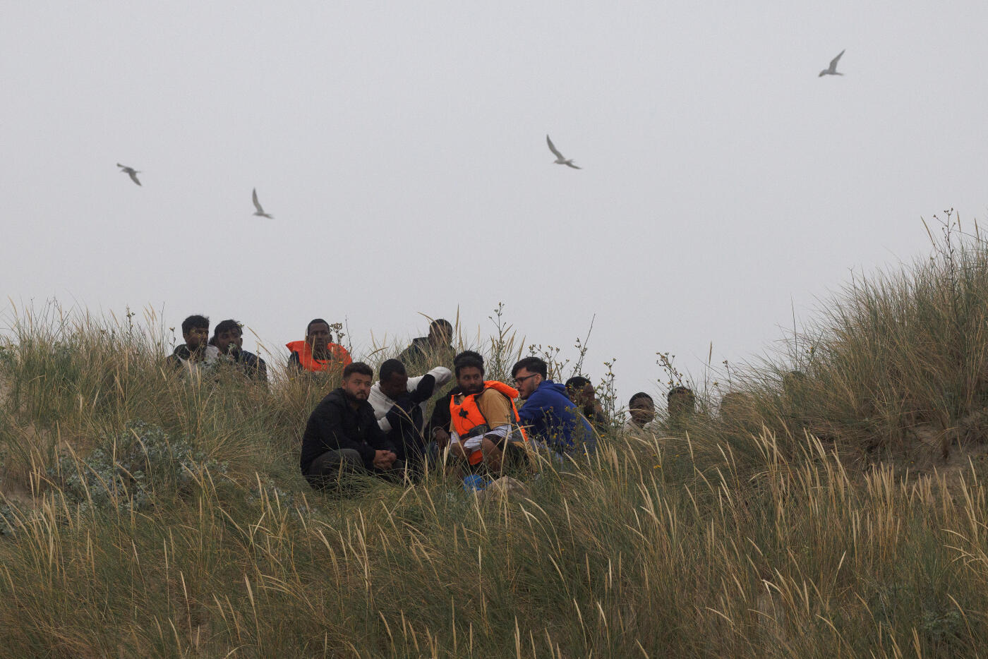 GRAVELINES, FRANCE - JULY 02: Migrants sit in the dunes waiting for a small boat to collect them on July 02, 2025 in Gravelines, France. The boat eventually arrived through the fog, already very full of migrants who had boarded further down the coast, looking to squeeze a few more people in. Last month, it was reported that French officials were planning changes to policies that govern interceptions at sea, allowing police to intercept small boats within 300 metres of the French shoreline, in a bid to curb migrant crossings of the English Channel. The move, which has not been confirmed, would be welcomed by UK authorities, who see it as a step toward stronger border enforcement. (Photo by Dan Kitwood/Getty Images)