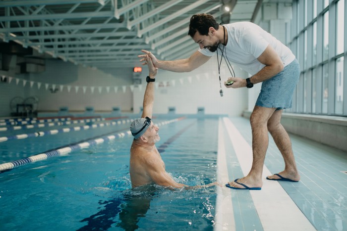 Personal coach encouraging swimmer when swimming indoors in swimming pool.