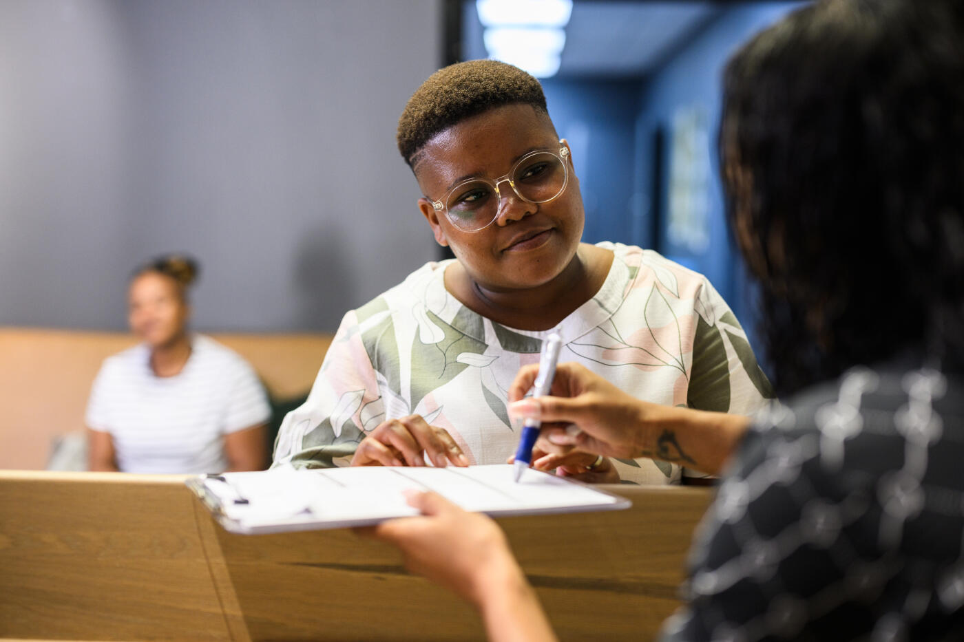 Over shoulder view receptionist explaining form to LGBTQIA woman in medical clinic