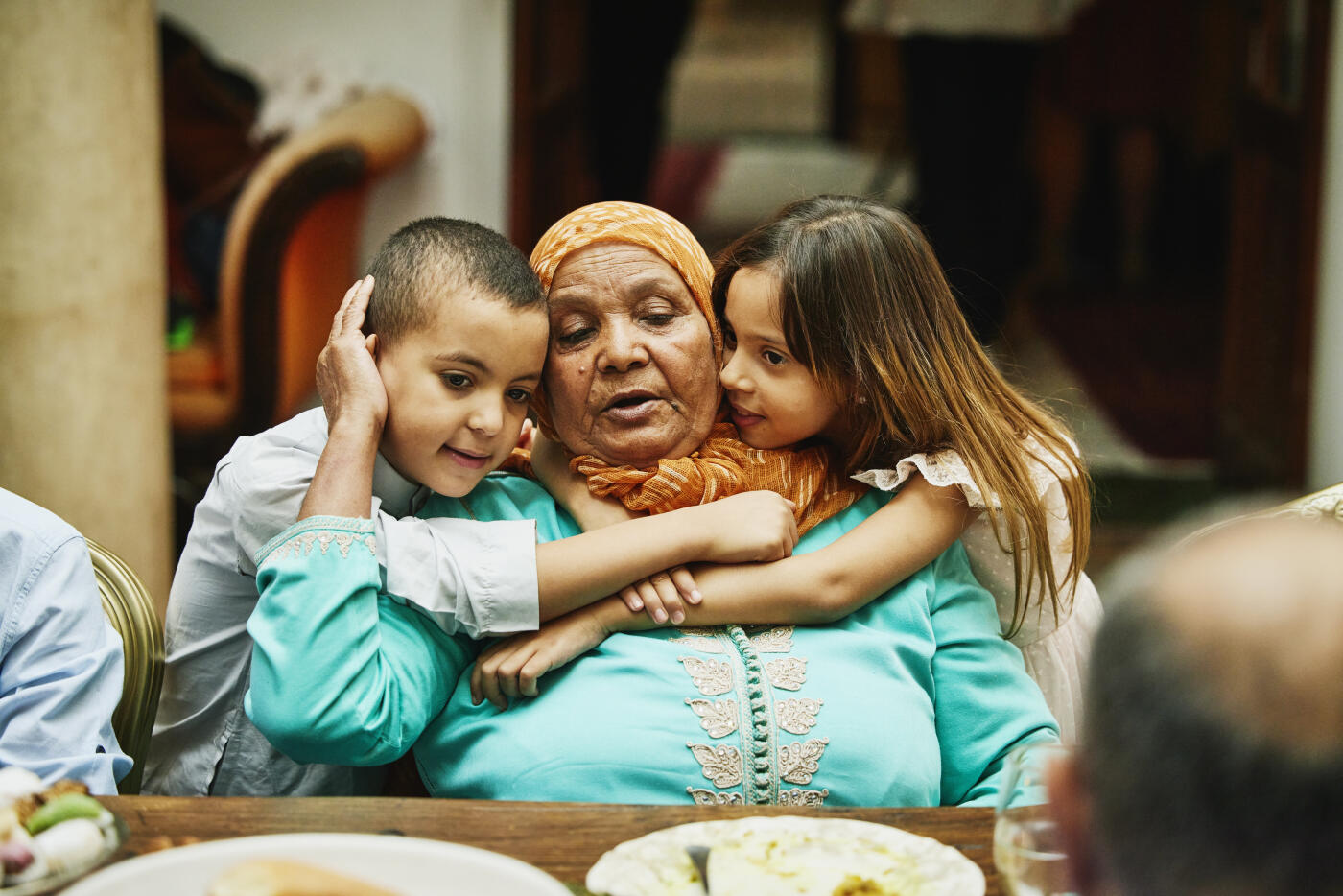 Medium shot of granddaughter and grandson hugging grandmother during multigenerational family celebration dinner