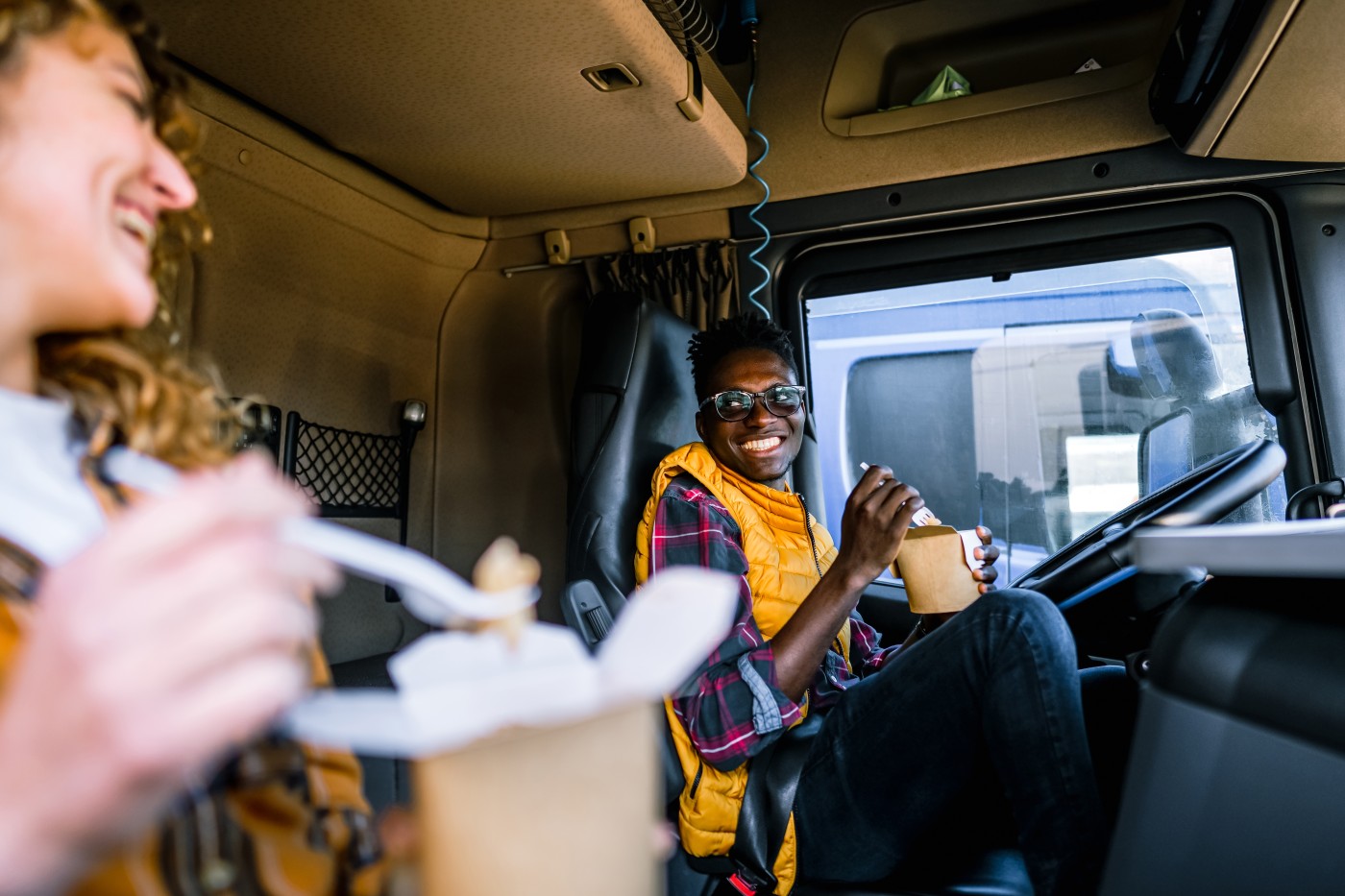 Female and male truck drivers eating a takeaway meal on lunch break in truck's cabin