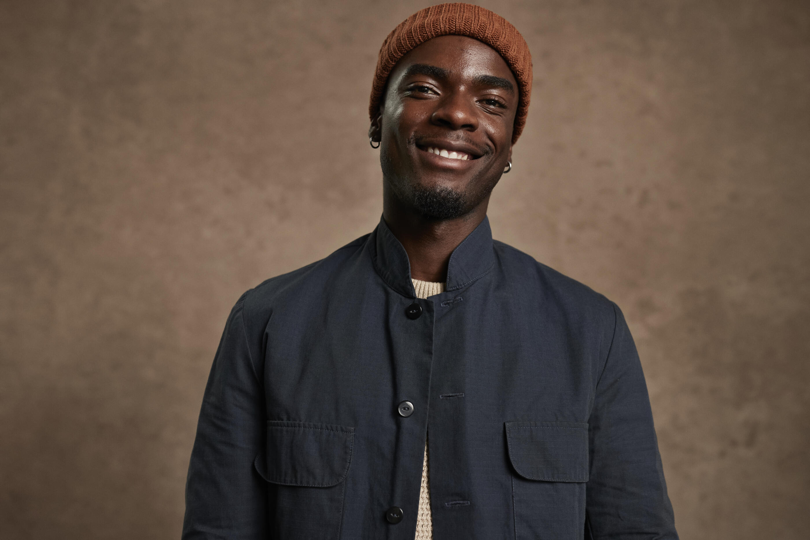 Portrait of smiling young man wearing knit hat against brown background