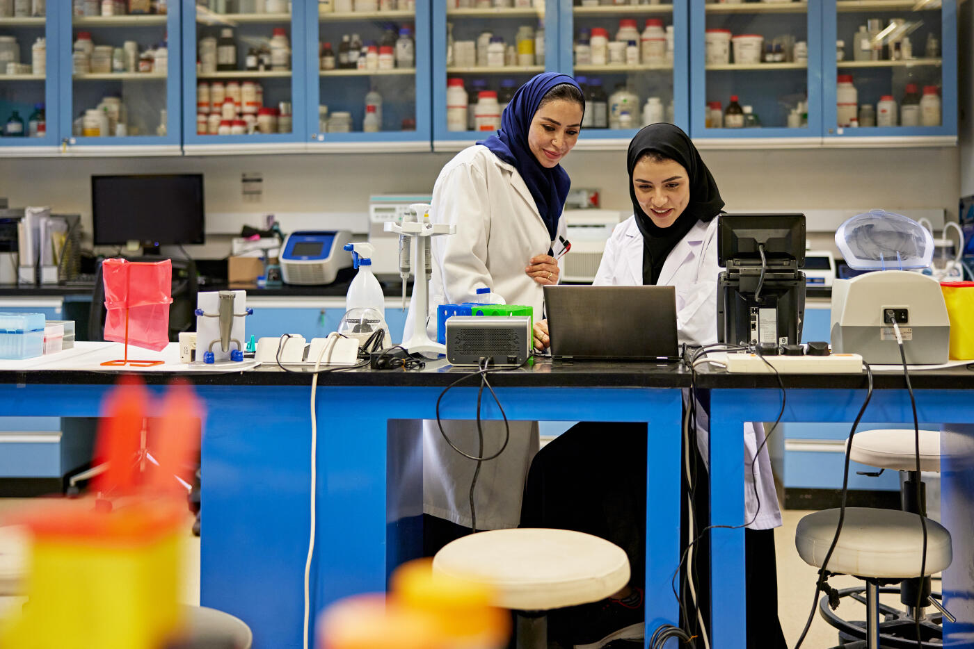 Smiling female teacher assisting student doing research sitting in science lab in Saudi university