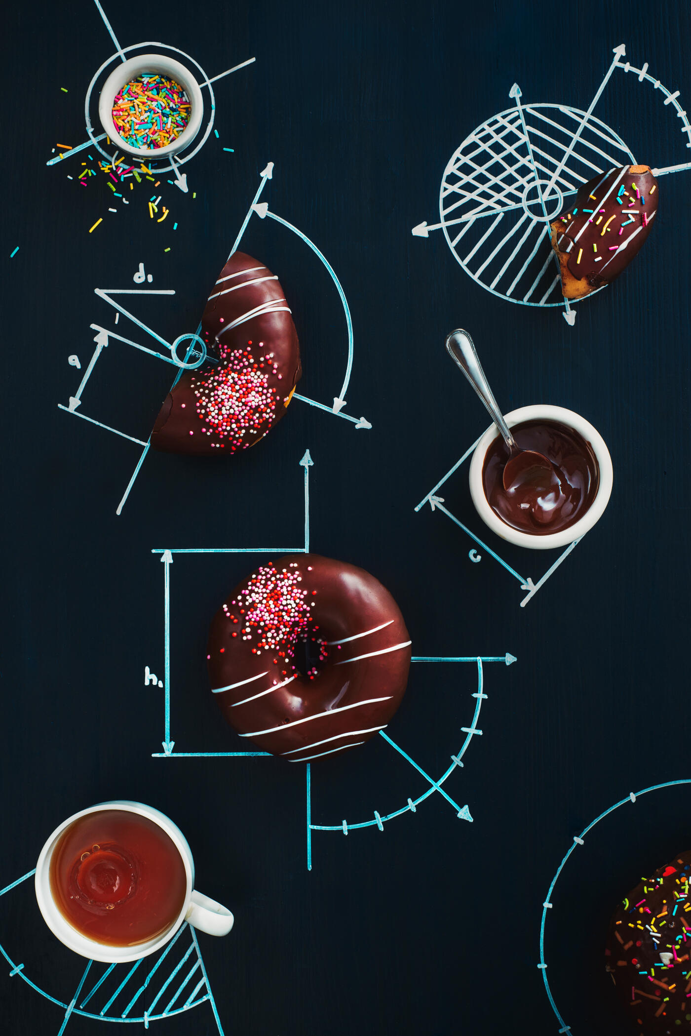 A whole donut and a half of a donut with chocolate icing and pink sprinkles on a blackboard with geometrical drawings.