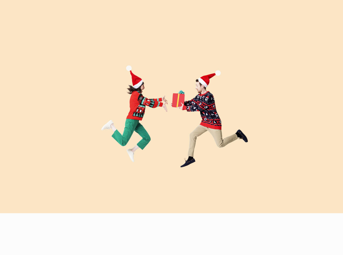 man and woman in santa hat and Christmas sweater giving presents in mid air against cream background