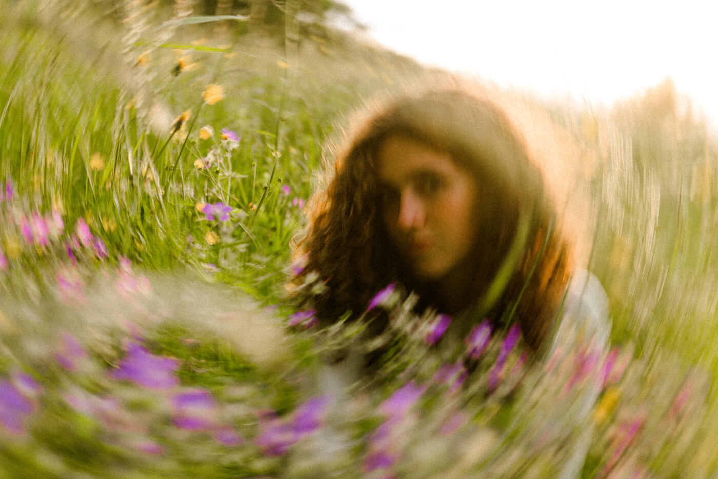 A hazy portrait of a young woman in a vibrant flower field. The image features a circular blur, creating a dreamy, nature-inspired mood. Part of a series with video