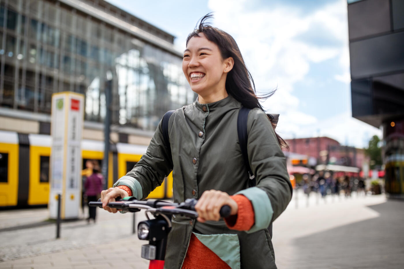 Cheerful young woman riding push scooter in city during vacation
